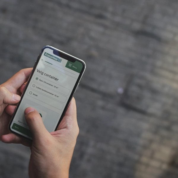 Bilde av person som holder mobil med nettside til Franzefoss. Velger container. Foto