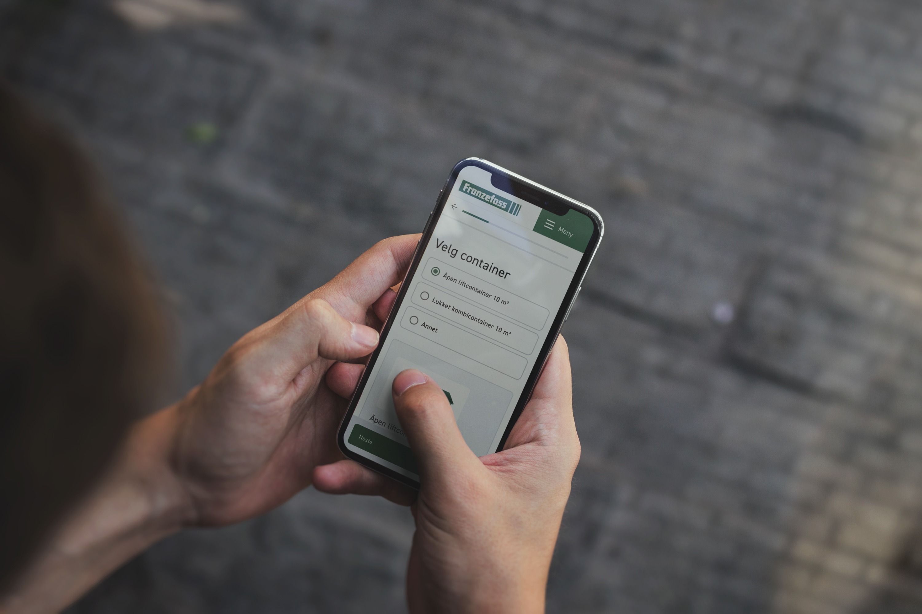 Bilde av person som holder mobil med nettside til Franzefoss. Velger container. Foto