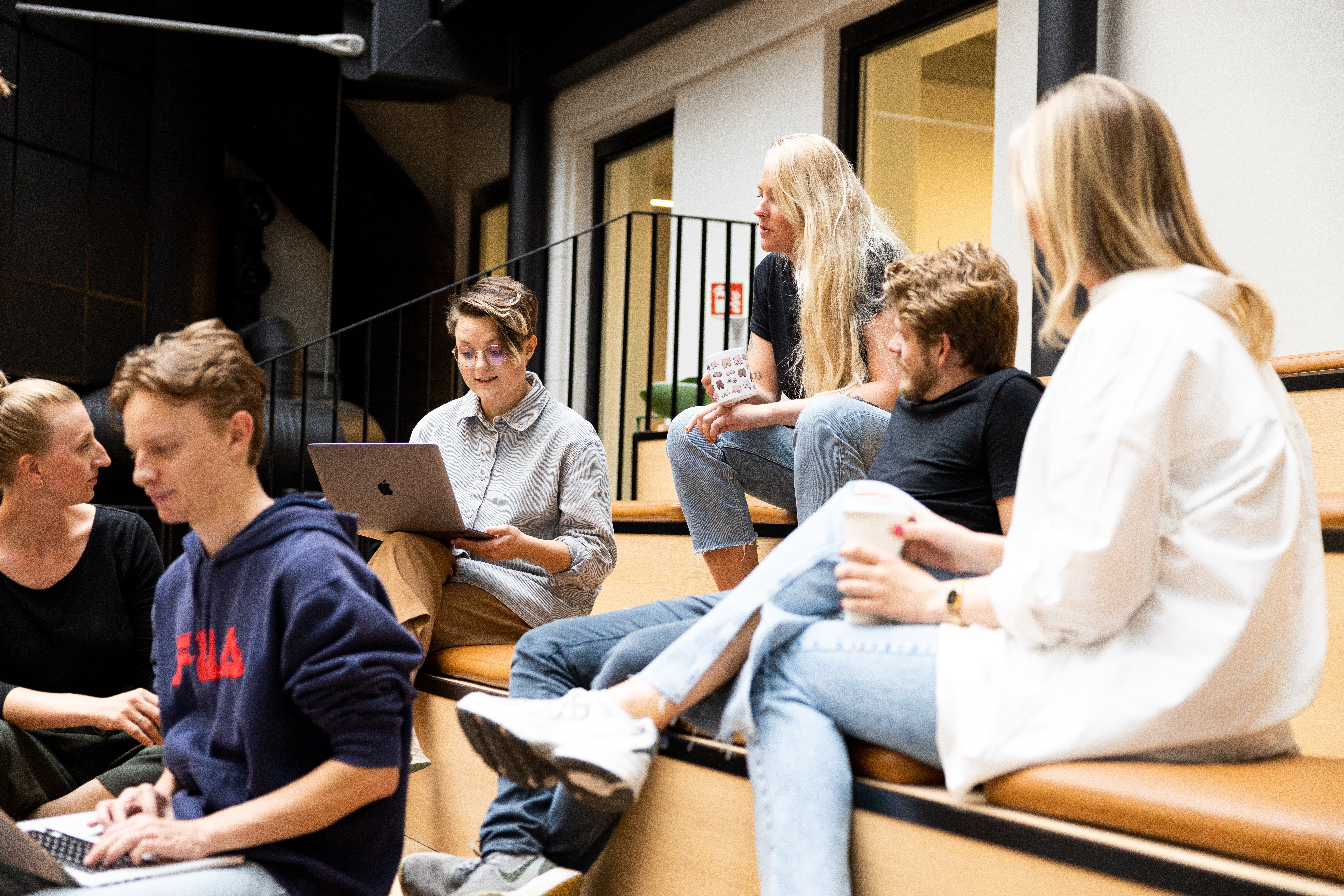 en gruppe mennesker sitter på trappene og bruker bærbare datamaskiner.