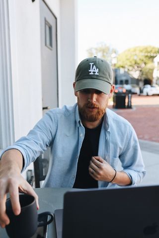 Mann sitter utenfor huset med laptop og kaffekopp. Foto