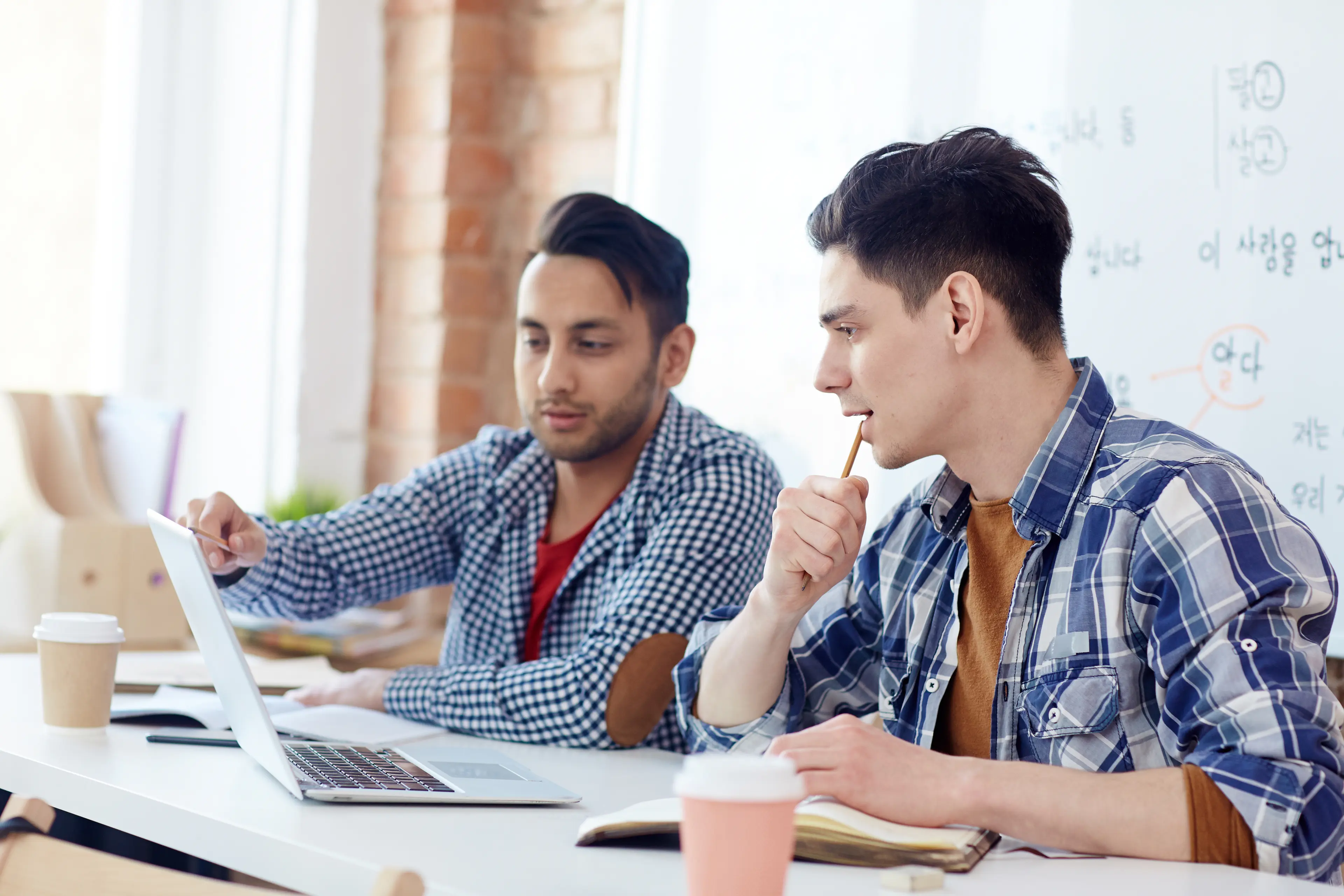 two men sitting at a table with laptops