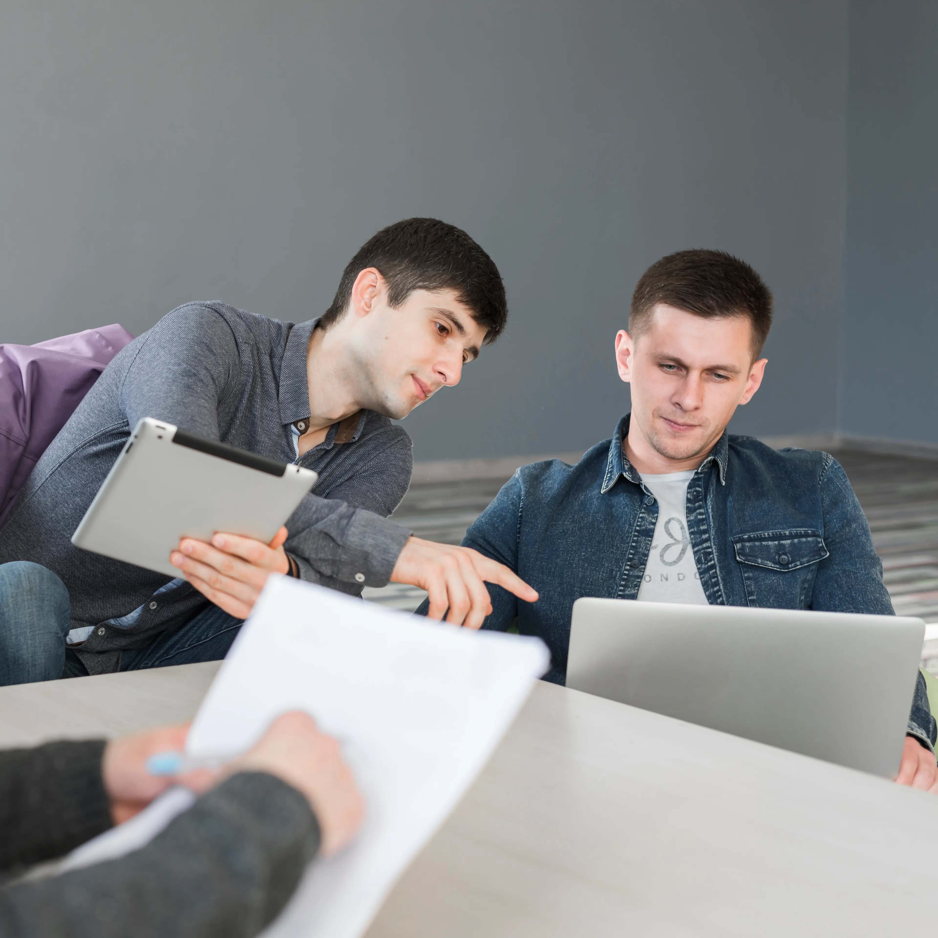 two men sitting at a table looking at a laptop