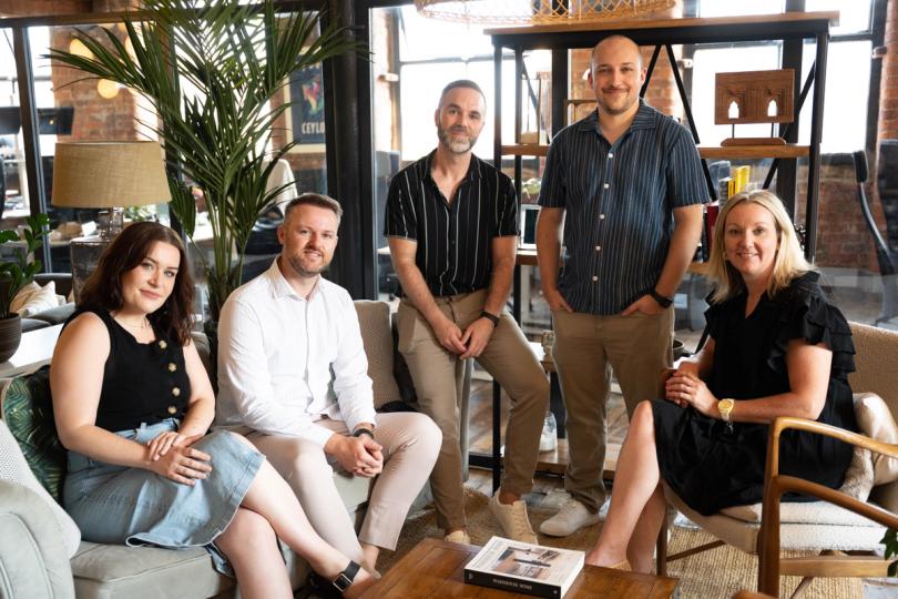 Five members of the Tank team sit, smiling, in a row in the Manchester office.