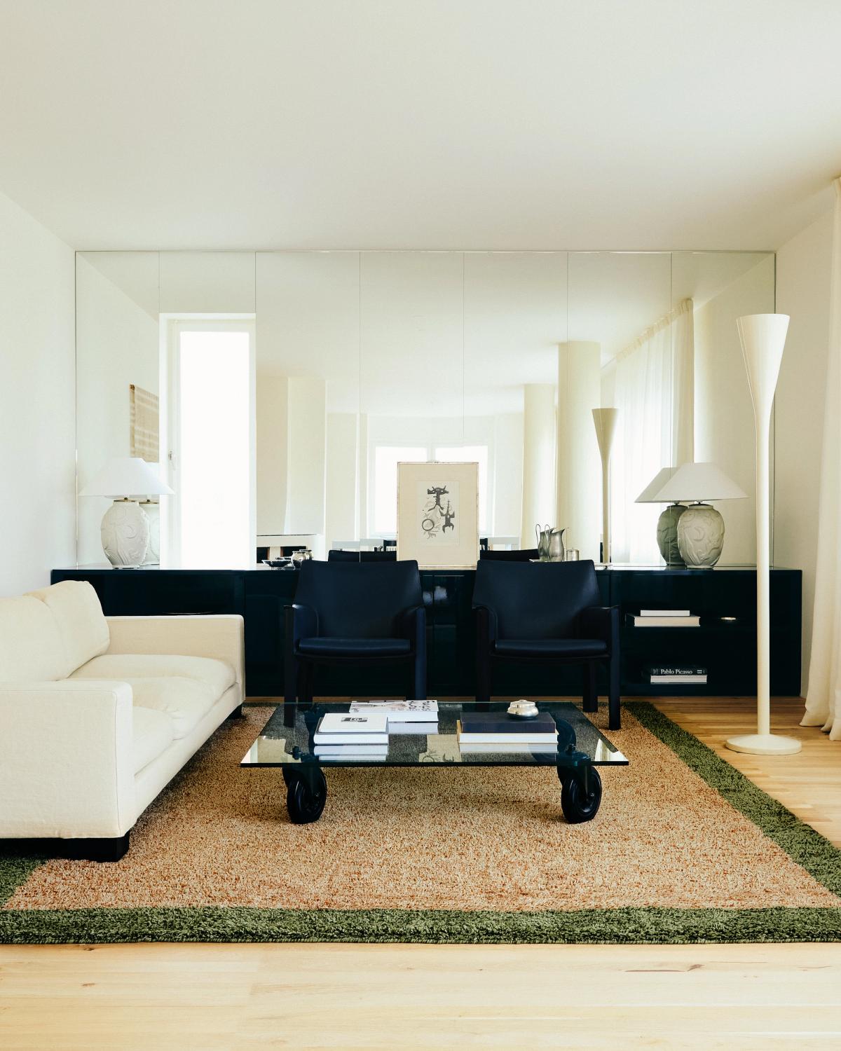 Shaggy wool rug Ryya in Beige pictured in a brightly lit living room with black interior design details and a white sofa.