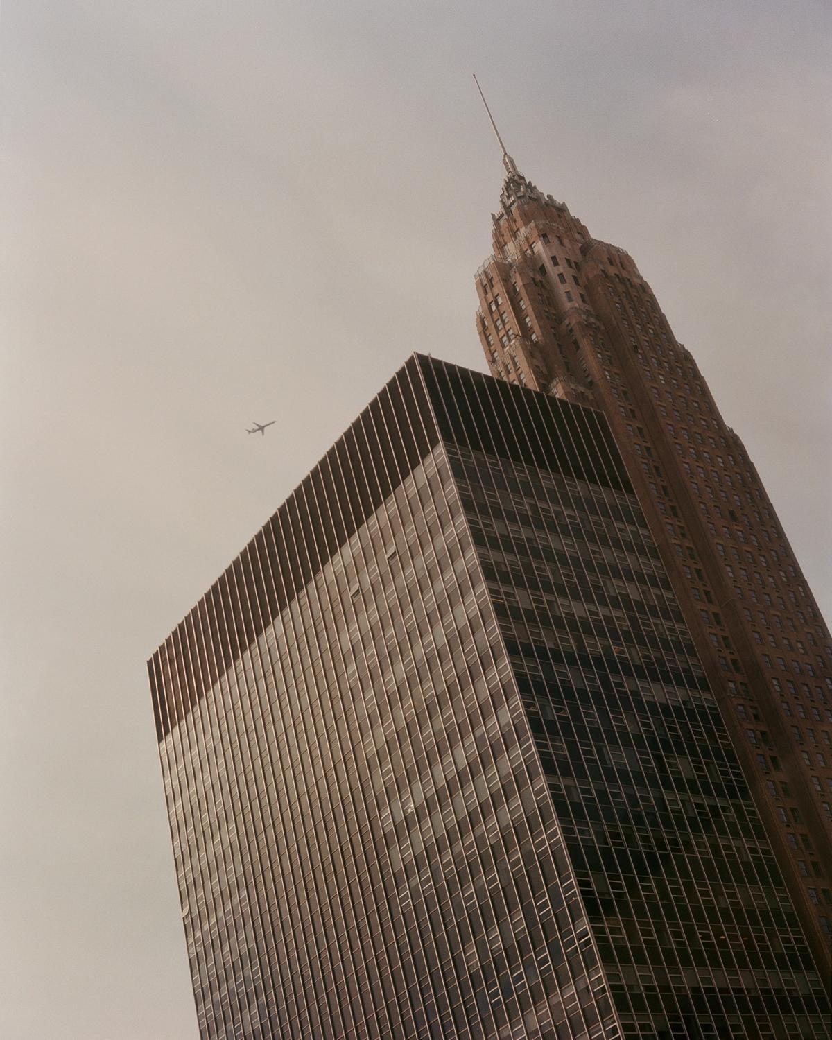 A high-rise building in New York shot from below as a plane flies by.