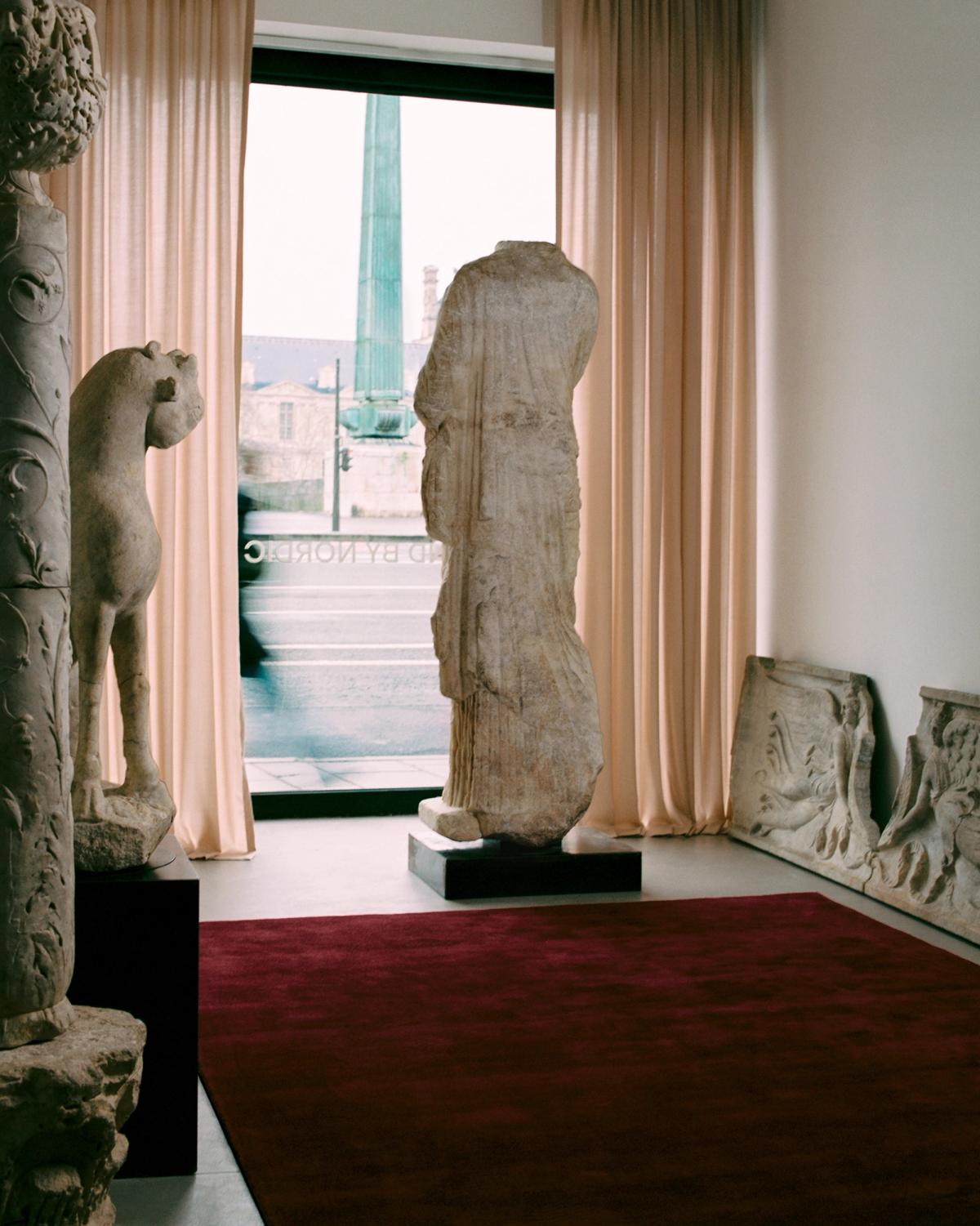 The Grand rug in Deep Wine displayed in a room with sculptures, with soft light filtering through the Grand curtain in Old Rose.