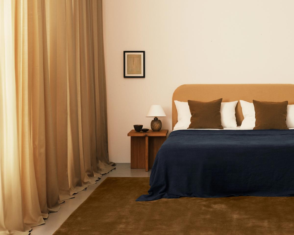 Les rideaux Grand Leo photographiés à côté d’un lit moelleux dans une chambre aux détails de décoration intérieure orange et bleus.