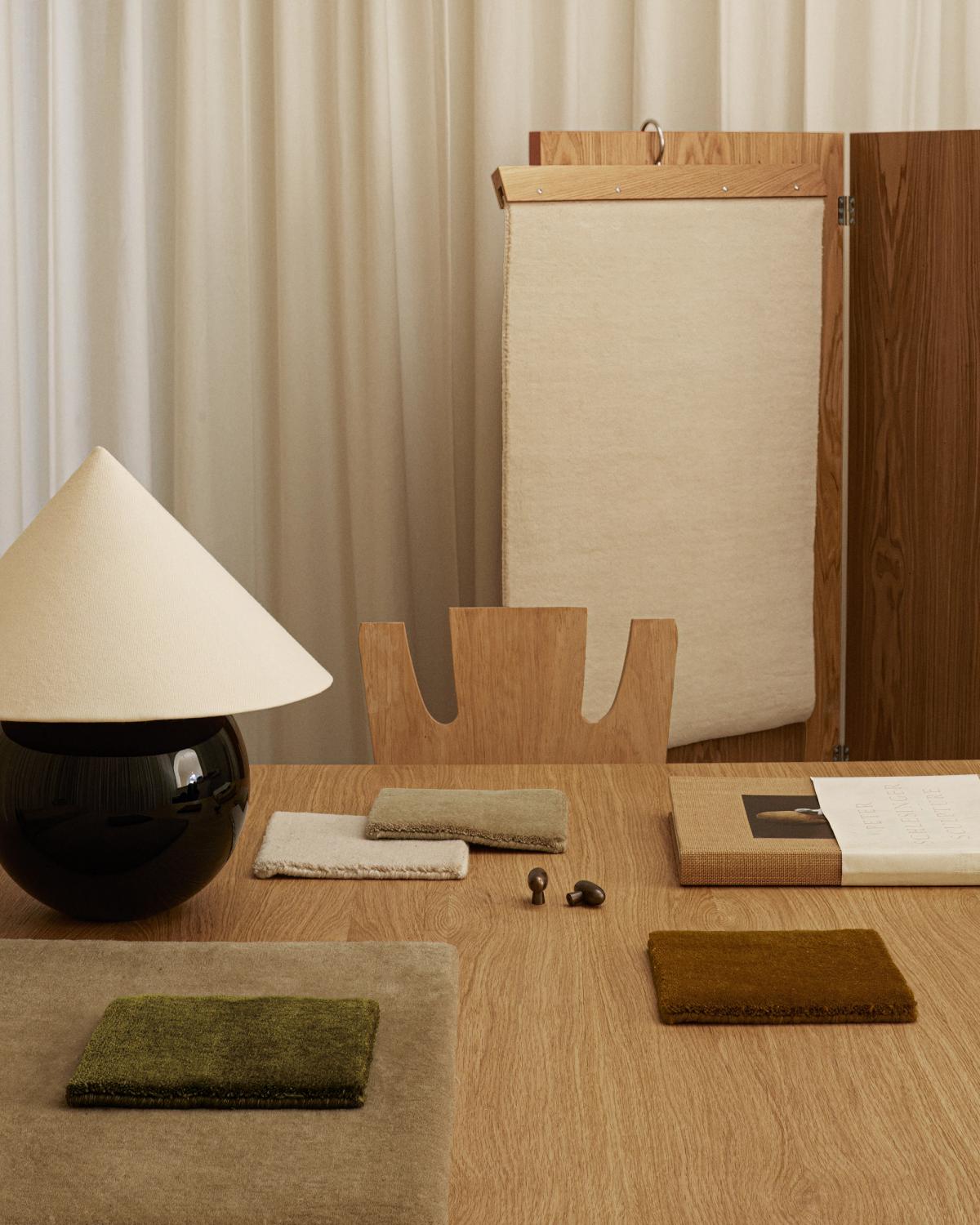 Muster des flauschigen Wollteppichs Grand in verschiedenen Farben, abgebildet auf einem Holztisch in einem modernen Büroraum.