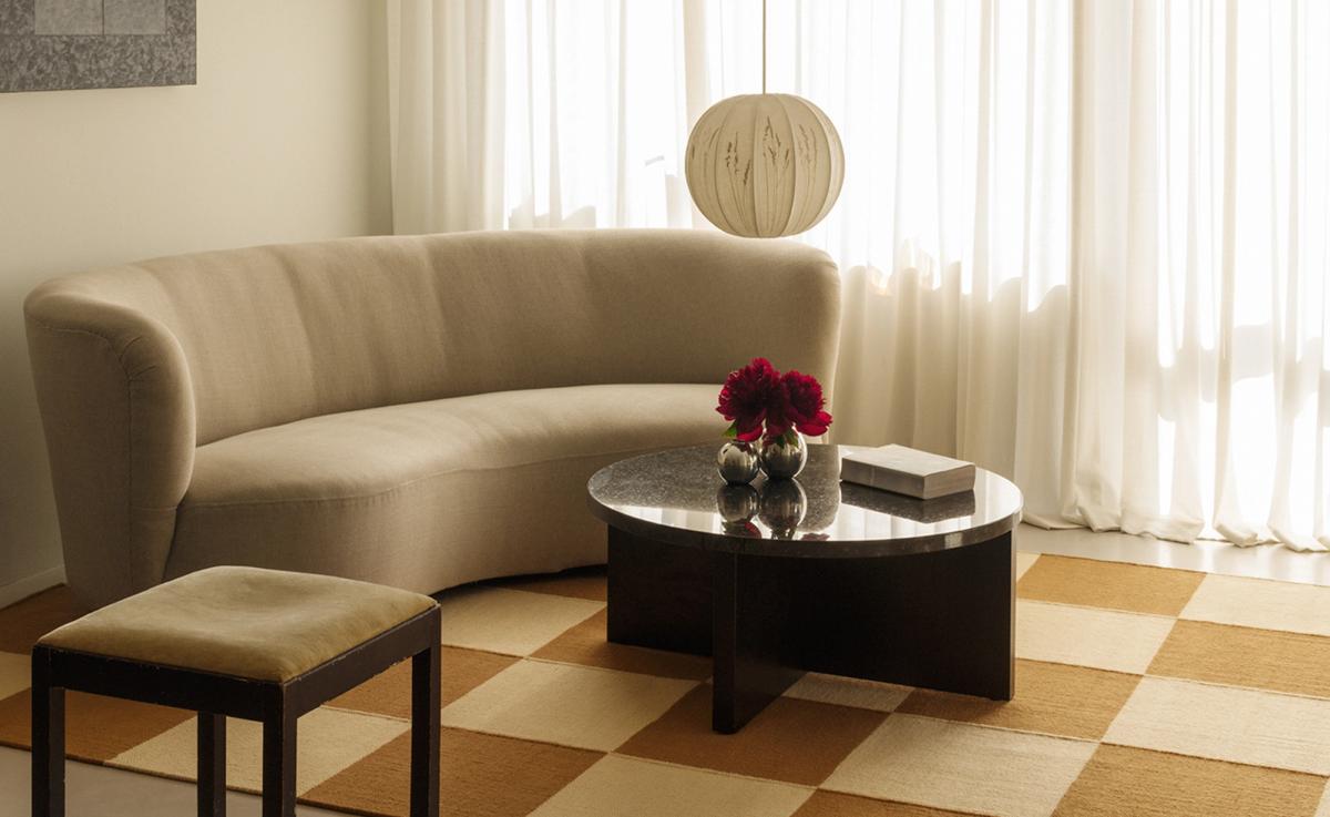 Square – Leo/Yellow sets the tone with its bold checkered design in warm neutrals. A curved cream sofa, sculptural black stone coffee table, and vintage wood-framed stool bring balance and softness to the graphic grid, while sheer curtains diffuse the daylight with quiet elegance.