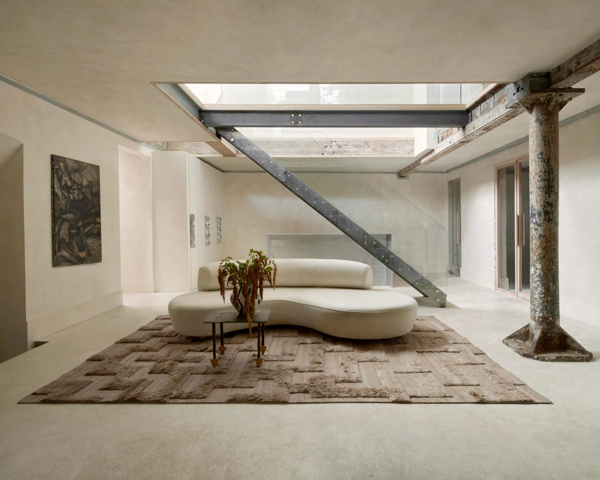 Der Boho-Teppich in Brown verleiht einem minimalistischen Loft reichhaltige Textur und Tiefe – kombiniert mit rohen Balken, Betonboden und einem skulpturalen cremefarbenen Sofa.