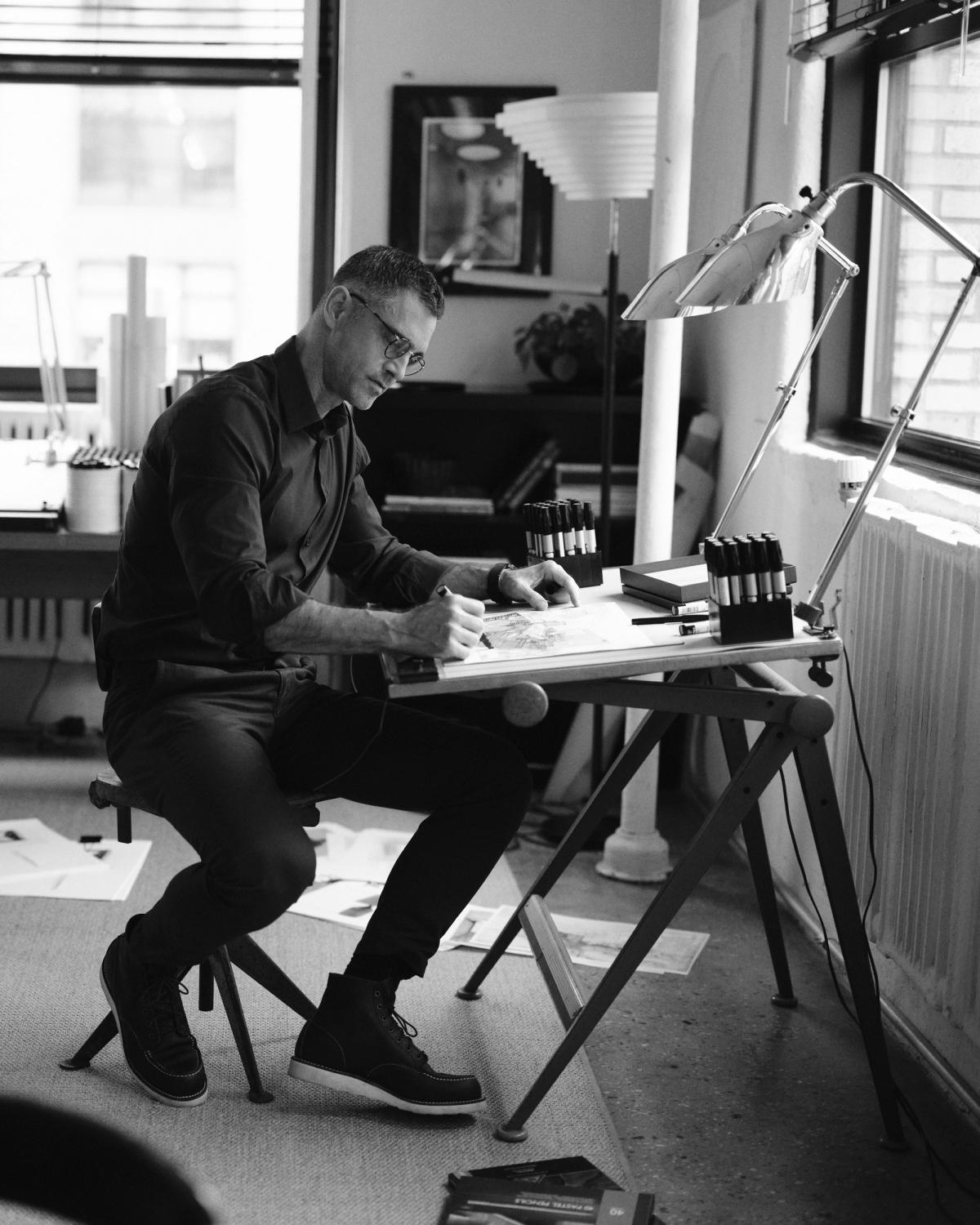 En formgivare sittande i en studio i Soho, New York, omgiven av skisser, verktyg och materialprover.