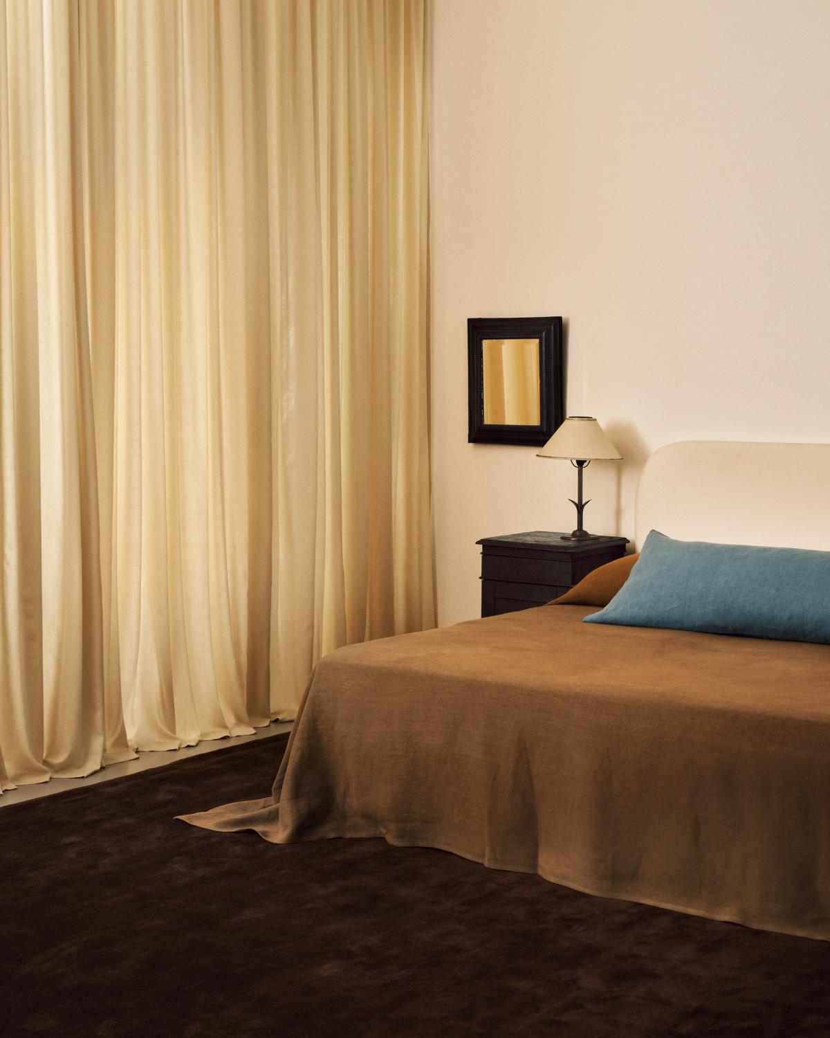 Les rideaux The Grand Sunrise photographiés dans une chambre avec des détails d’intérieur dans les tons bruns et orange, accompagnés du tapis en laine moelleux Grand Walnut.