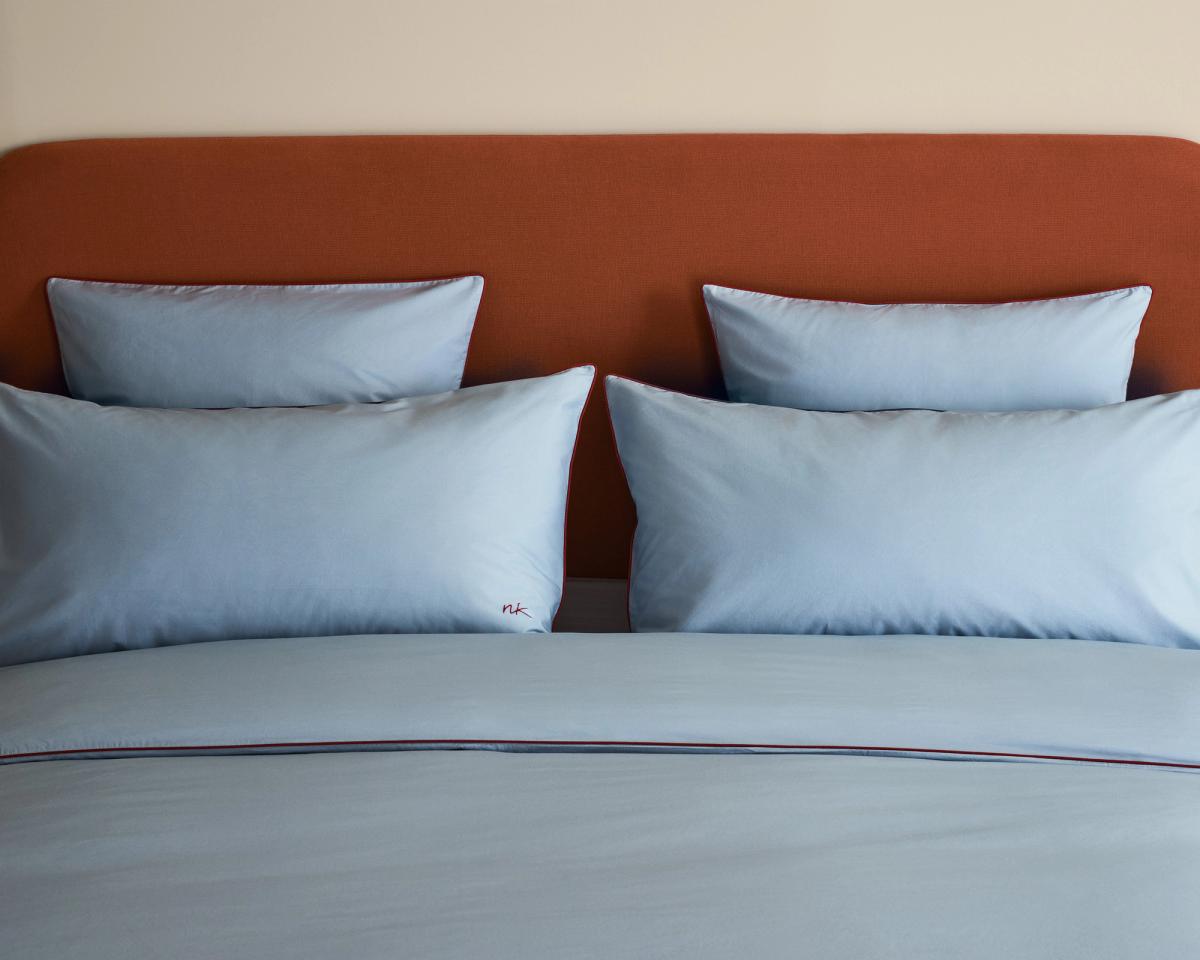 Bett mit dem Signature Headboard in Burnt Red, bezogen mit der Percale Bedding Collection in Shirt Blue/Red.