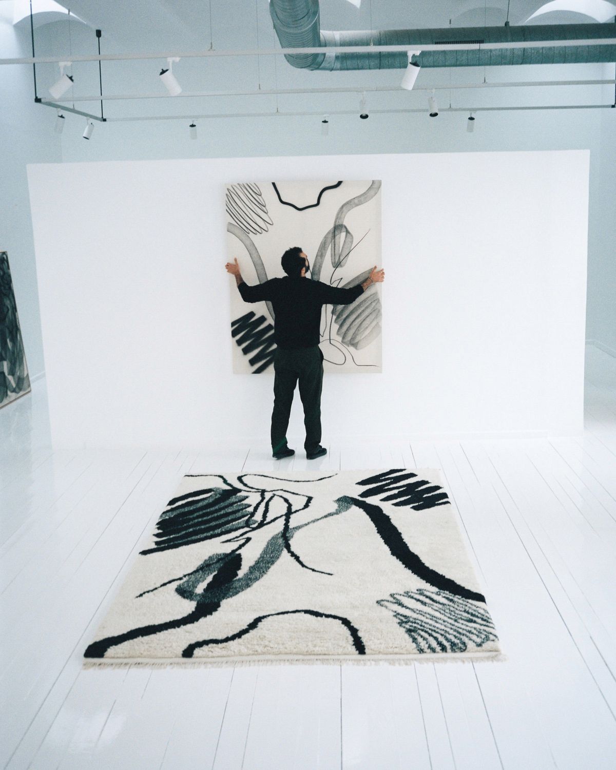 Aythamy Armas in his Barcelona studio hanging the painting and the rug laying on the floor.