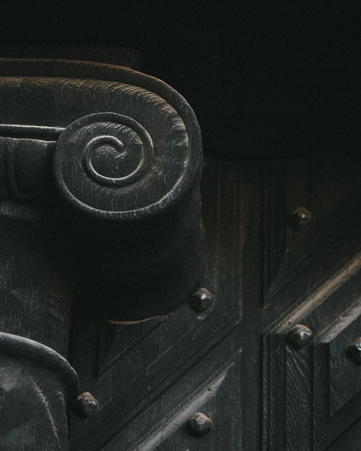 Gros plan sur un chapiteau ionique en bois sculpté, avec une patine visible et des détails de rivets.