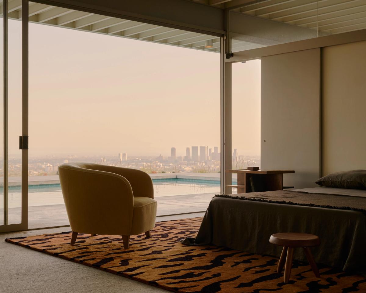 Tigris – Rust/Black bringt kräftigen Kontrast und wohltuende Wärme in dieses ruhige, moderne Schlafzimmer. Das markante Tigerstreifenmuster verankert den Raum unter einem senffarbenen Sessel und einem anthrazitfarbenen Bett. Fenster vom Boden bis zur Decke eröffnen einen Panoramablick auf Stadt und Pool, während sanftes Licht und natürliche Texturen eine ruhige, kuratierte Atmosphäre schaffen.