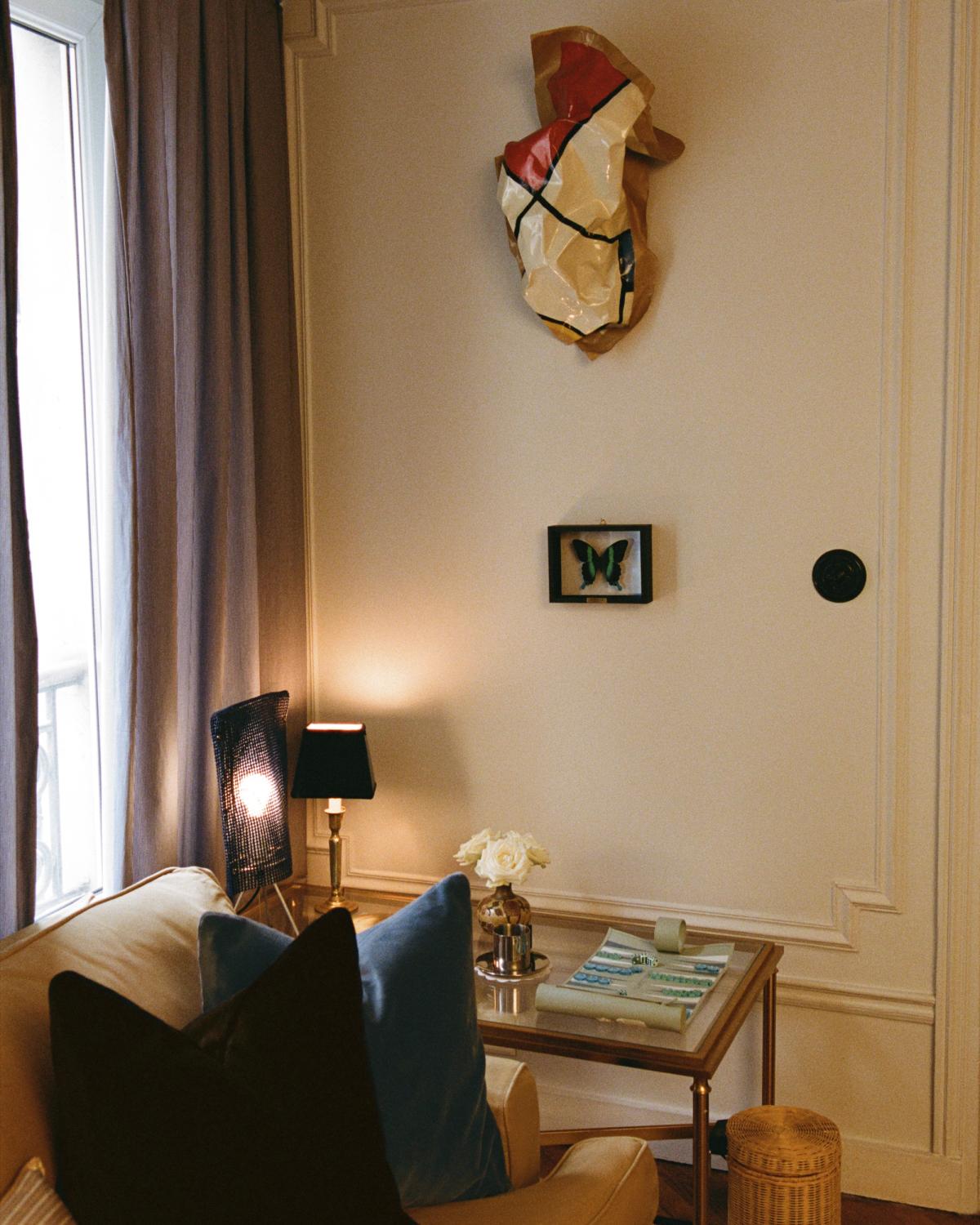 Die Teddy Velvet-Kissen in Mist und Walnut werden auf einem beigen Sofa in einer gemütlichen Ecke mit einem Glastisch, Büchern und einer Lampe gezeigt, vor einer sanft beleuchteten Wand mit gerahmter Kunst und neutralen Vorhängen.