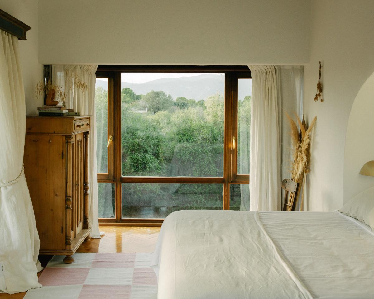 Square – Pink tillför mjuk geometri och mild färg till detta rofyllda sovrum. Mot bakgrund av naturträ, flödande gardiner och utsikt över en frodig trädgård ger det rutiga mönstret ett stillsamt inslag av lekfullhet och värme.