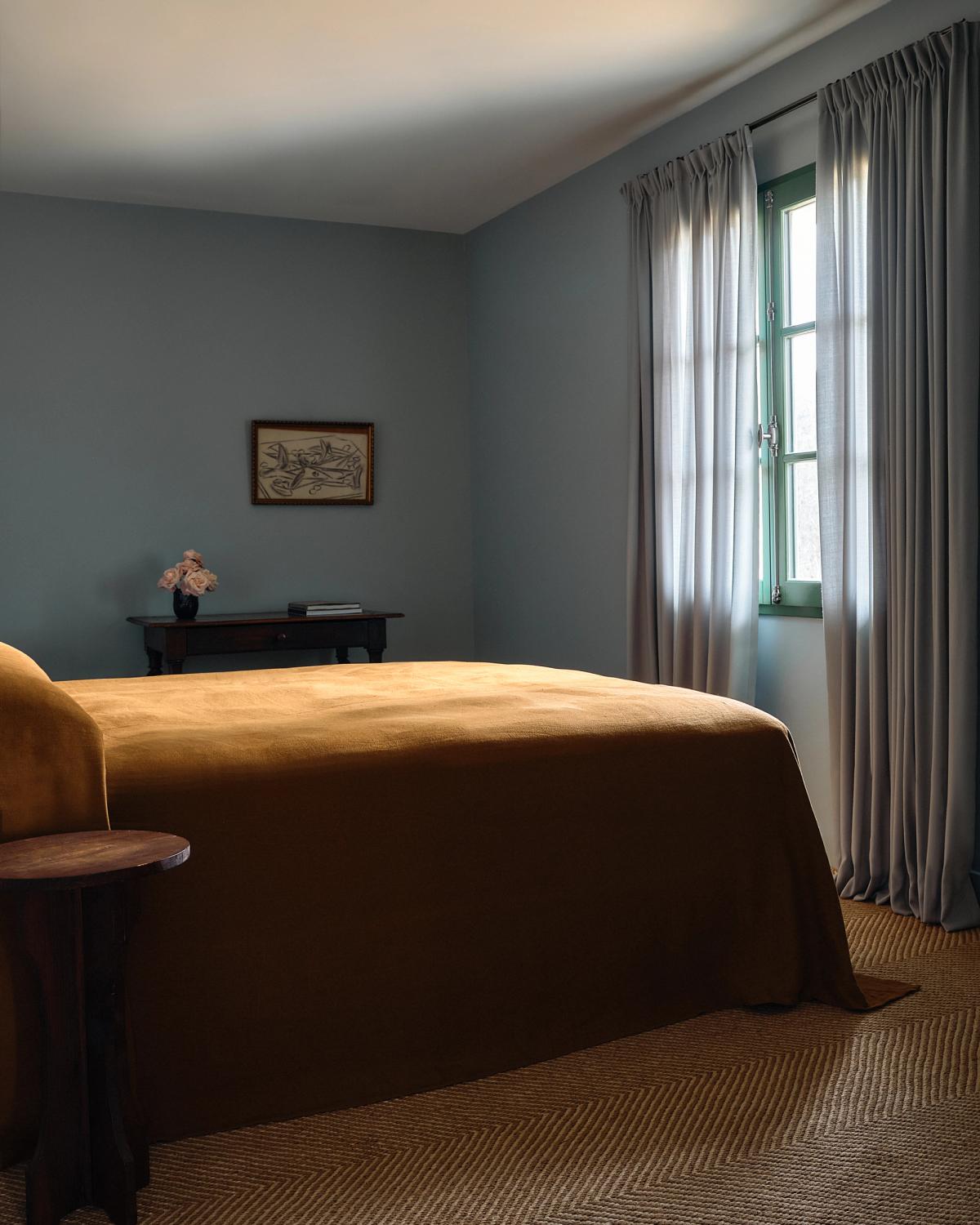 Vue large du tapis Jute Herringbone en Natural/Cream dans une chambre aux tons bleus, décorée avec des rideaux bleus, une table de chevet en bois et un arrangement floral.