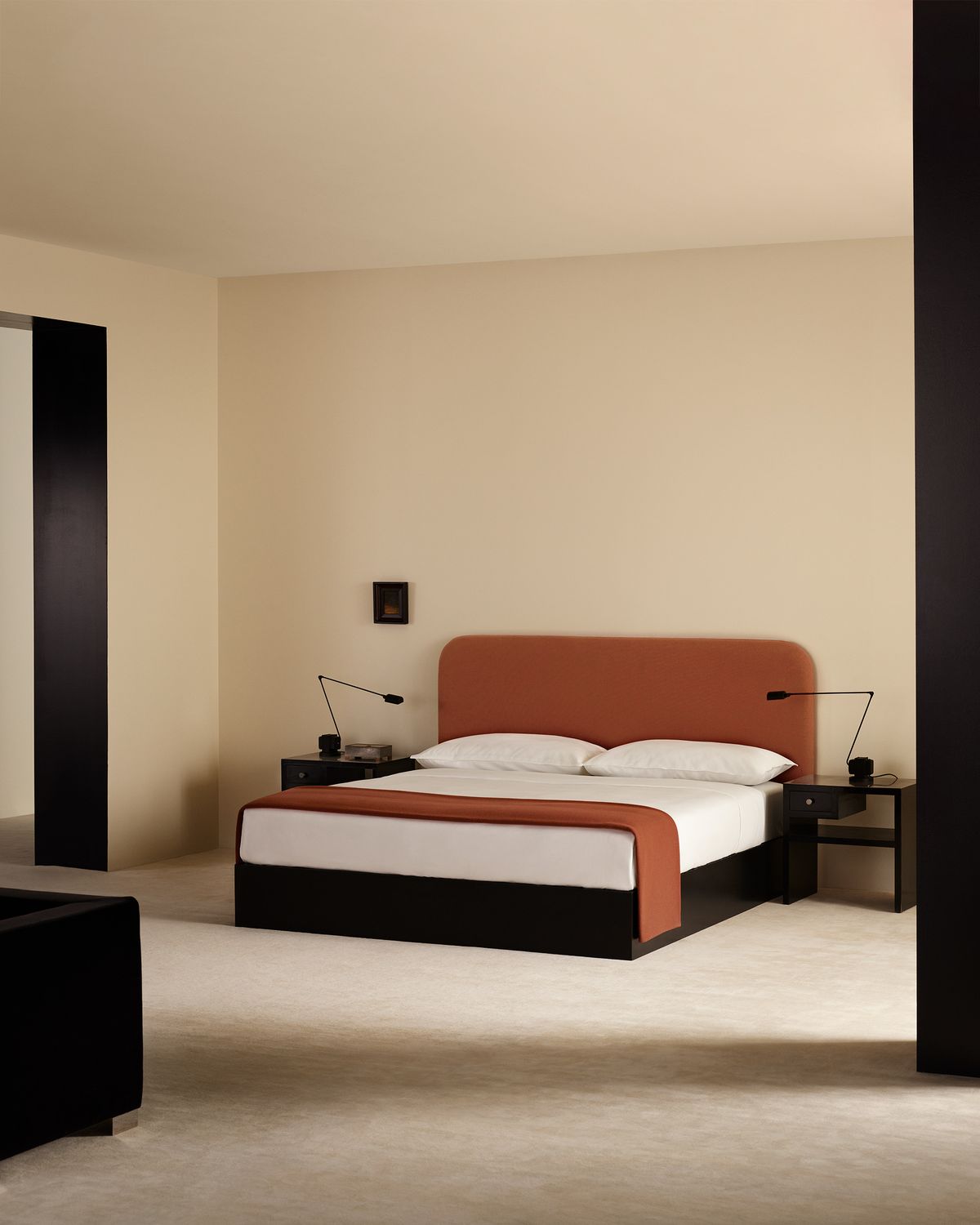 Heritage throw in Rust, styled on a bed with crisp white bedding and the Signature Headboard in Burnt Red, photographed in a minimalist bedroom with black side tables.