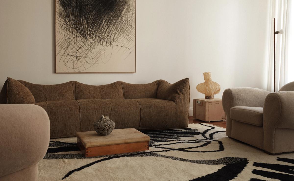 1212/21 av Aythamy Armas förankrar rummet med djärv, uttrycksfull rörelse i svart mot en mjuk elfenbensfärgad bas. I kombination med en mörkbrun texturerad soffa, skulpturala keramikföremål och lager av neutrala toner tillför mattan en grafisk kontrast till ett annars lugnt och taktilt rum.