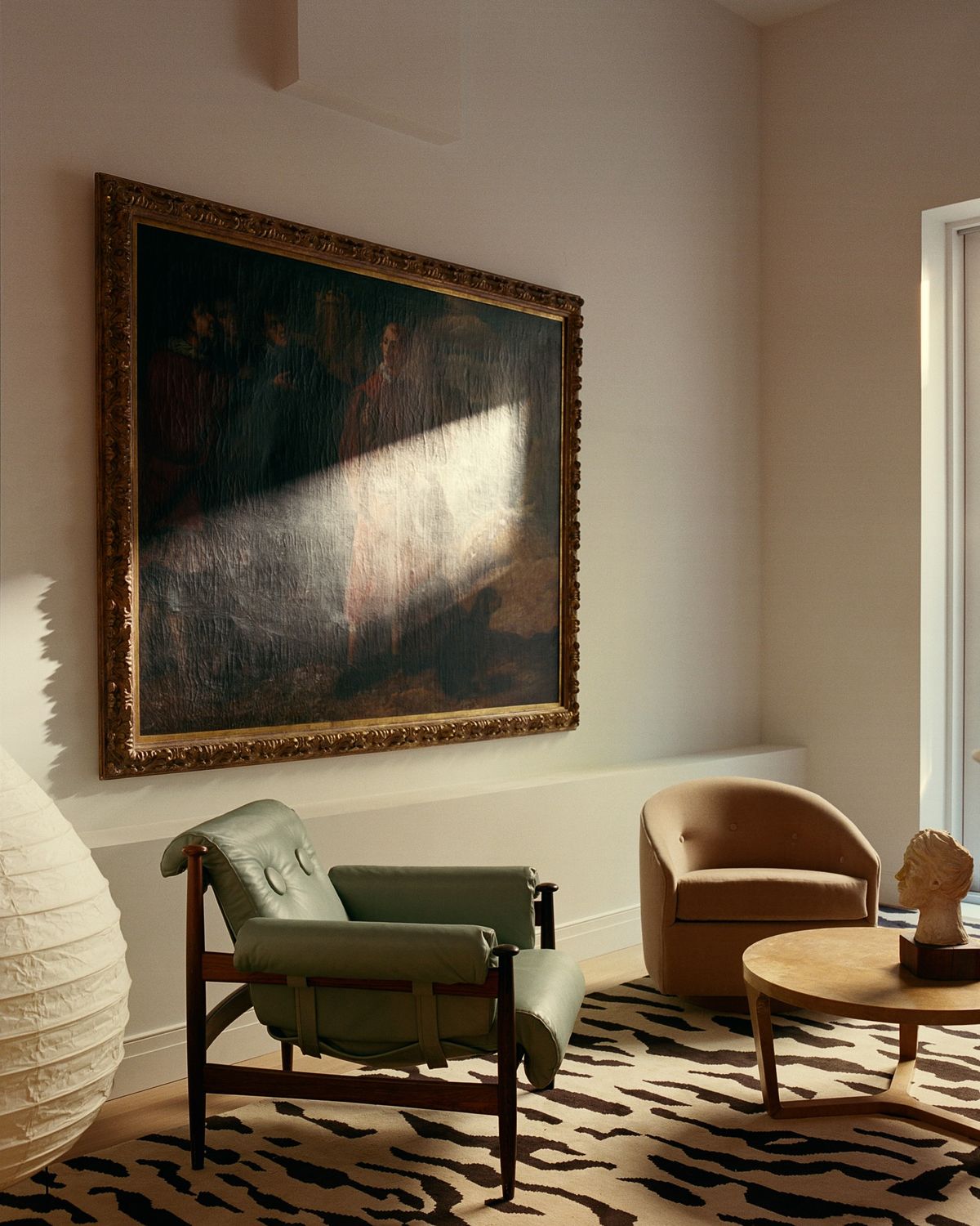 Tigris in Beige/Braun, das dem Raum unter einem Vintage-Gemälde eine grafische Weichheit verleiht – kombiniert mit skulpturalen Sitzmöbeln in warmen, sonnengeküssten Tönen.