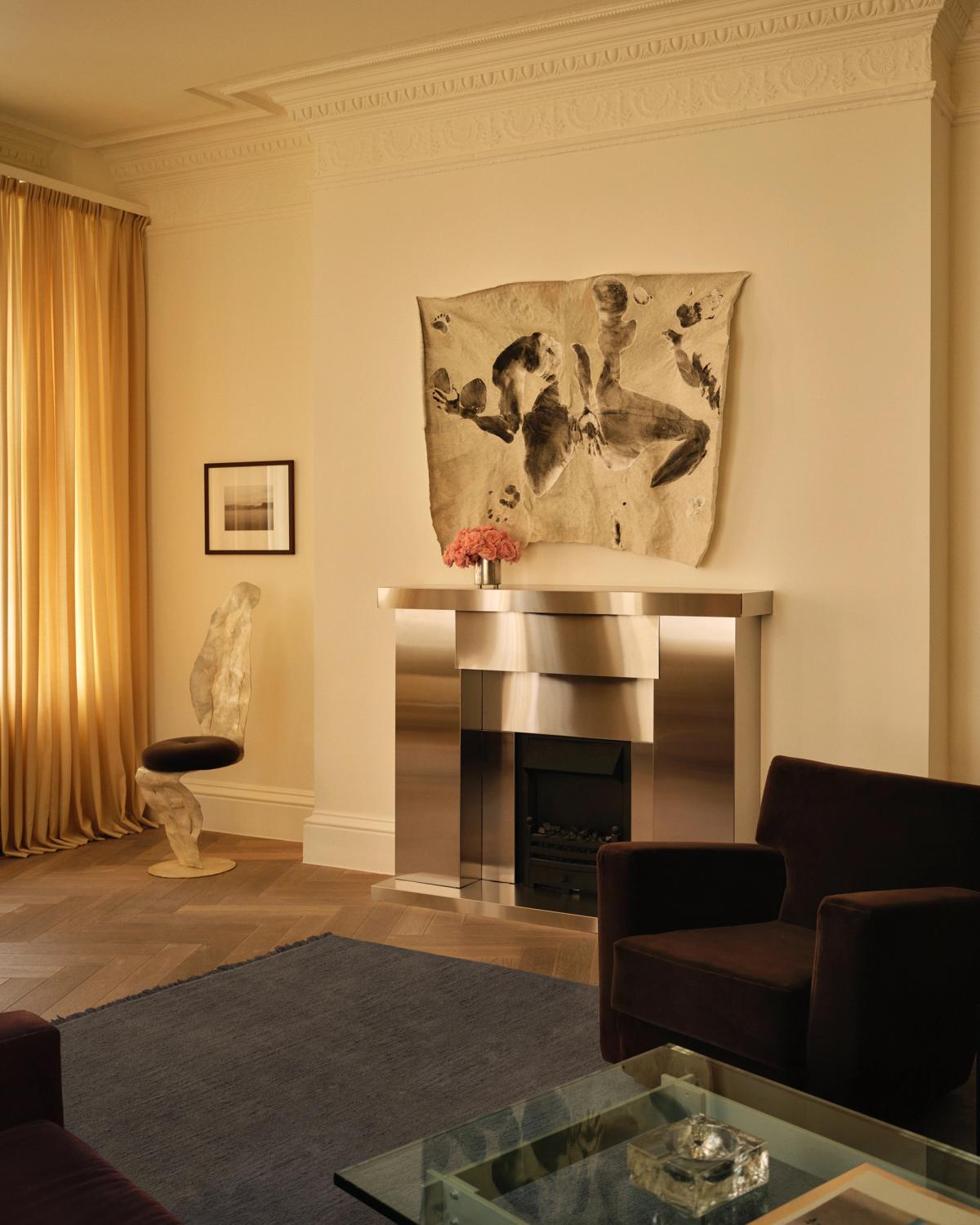 Le tapis Mohair en Slate Blue est présenté dans la boutique Nordic Knots de Mount Street à Londres, dans un salon raffiné avec des rideaux dorés, une cheminée métallique et un mobilier sculptural.