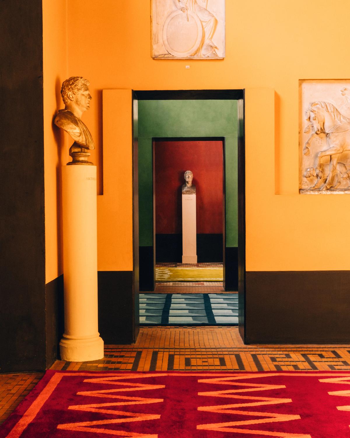 Campbell Rey 2023 collection plush wool rug Folding Ribbon - Burgundy photographed in a colorful room with beautiful art at Thorvaldsen Museum in Denmark.