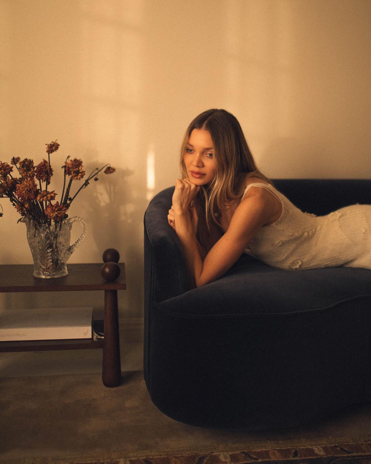 Jessie Andrews photographed on a blue velvet sofa with the plush wool rug Grand - Chestnut underneath.