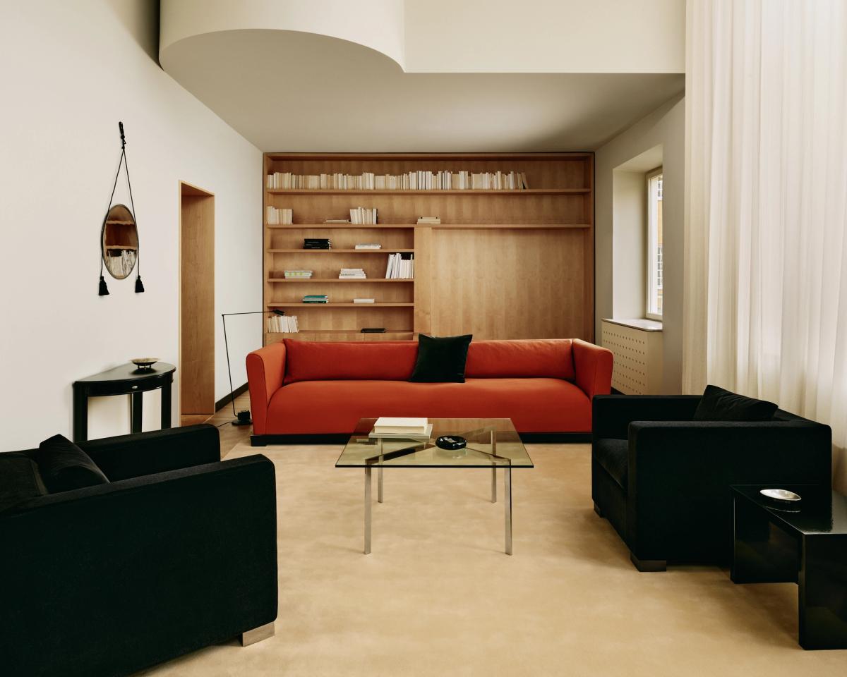 Tapis Grand en coloris Butter présenté dans un salon lumineux avec un canapé orange vif, deux fauteuils en velours noir et une table basse en verre à Stockholm, Suède.