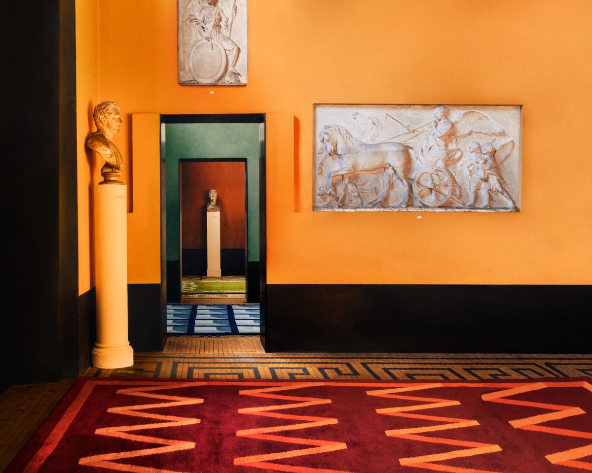 Tapis en laine moelleux Folding Ribbon - Burgundy de la collection 2023 de Campbell Rey, photographié dans une pièce colorée avec de magnifiques œuvres d'art au musée Thorvaldsen au Danemark.