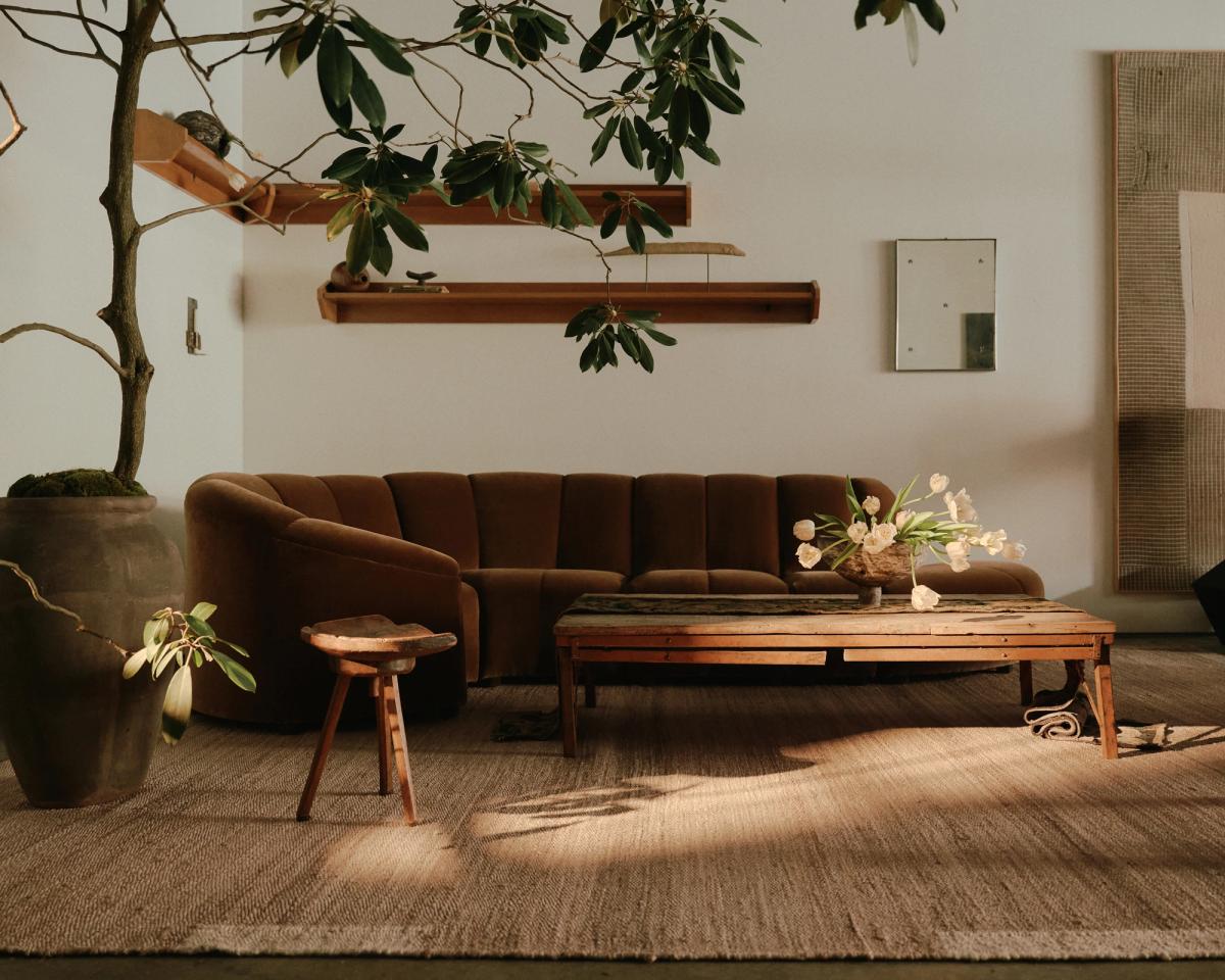 Tapis en jute Edge Cream photographié dans un salon chaleureux avec un mobilier aux tons neutres et de grandes plantes, au studio WAS à New York.