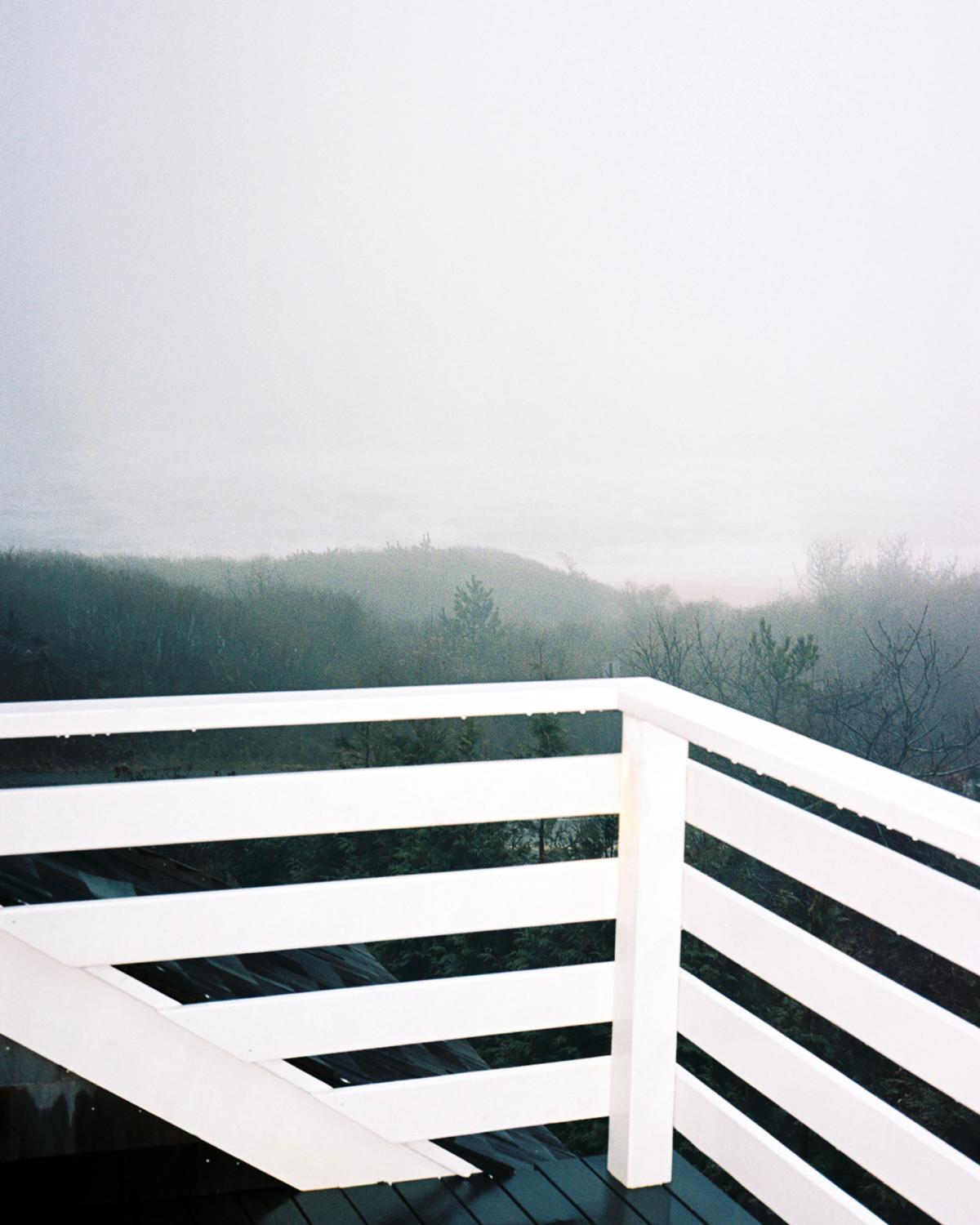 An image of a white railing, looking out over a foggy landscape.
