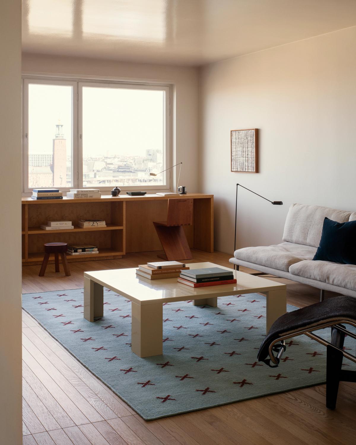 Cross rug in Blue/Burgundy featured in a light living room in Stockholm, Sweden. The flatweave rug is displayed underneath a yellow coffee table, next to a light gray sofa.