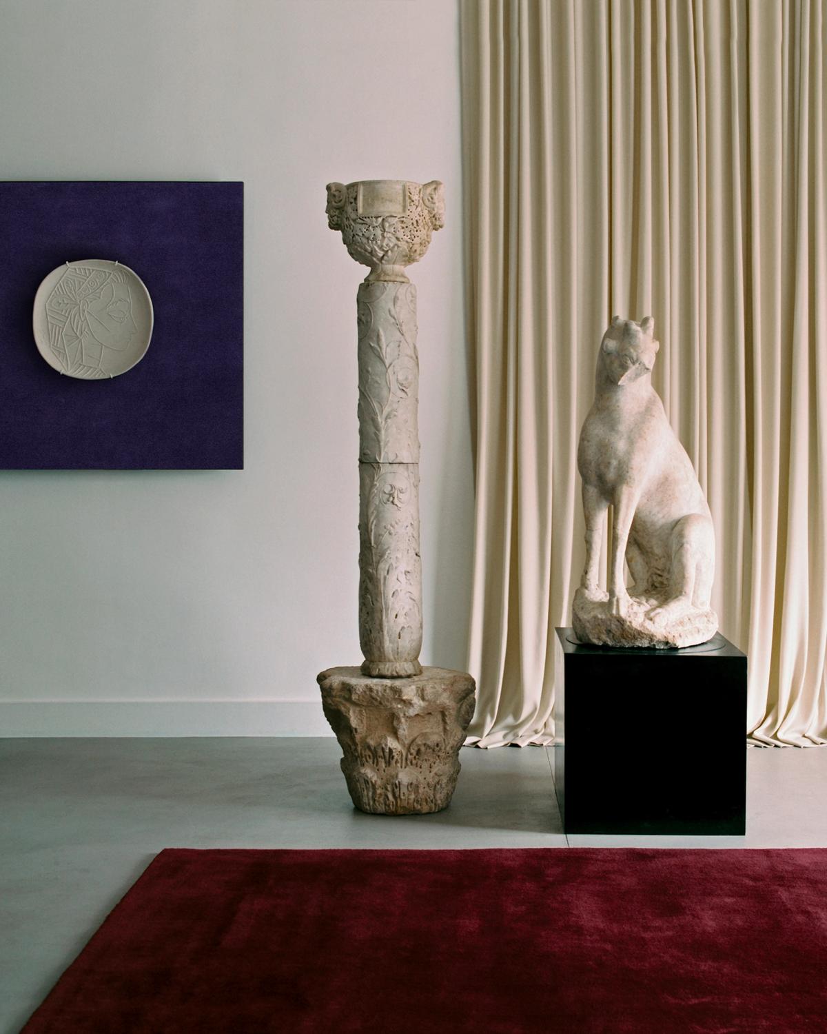 The Grand curtain in Pale Sand and the Grand rug in Deep Wine displayed in a room with sculptures, alongside a painting of the Grand rug in Lilac at Galerie Chenel in Paris.