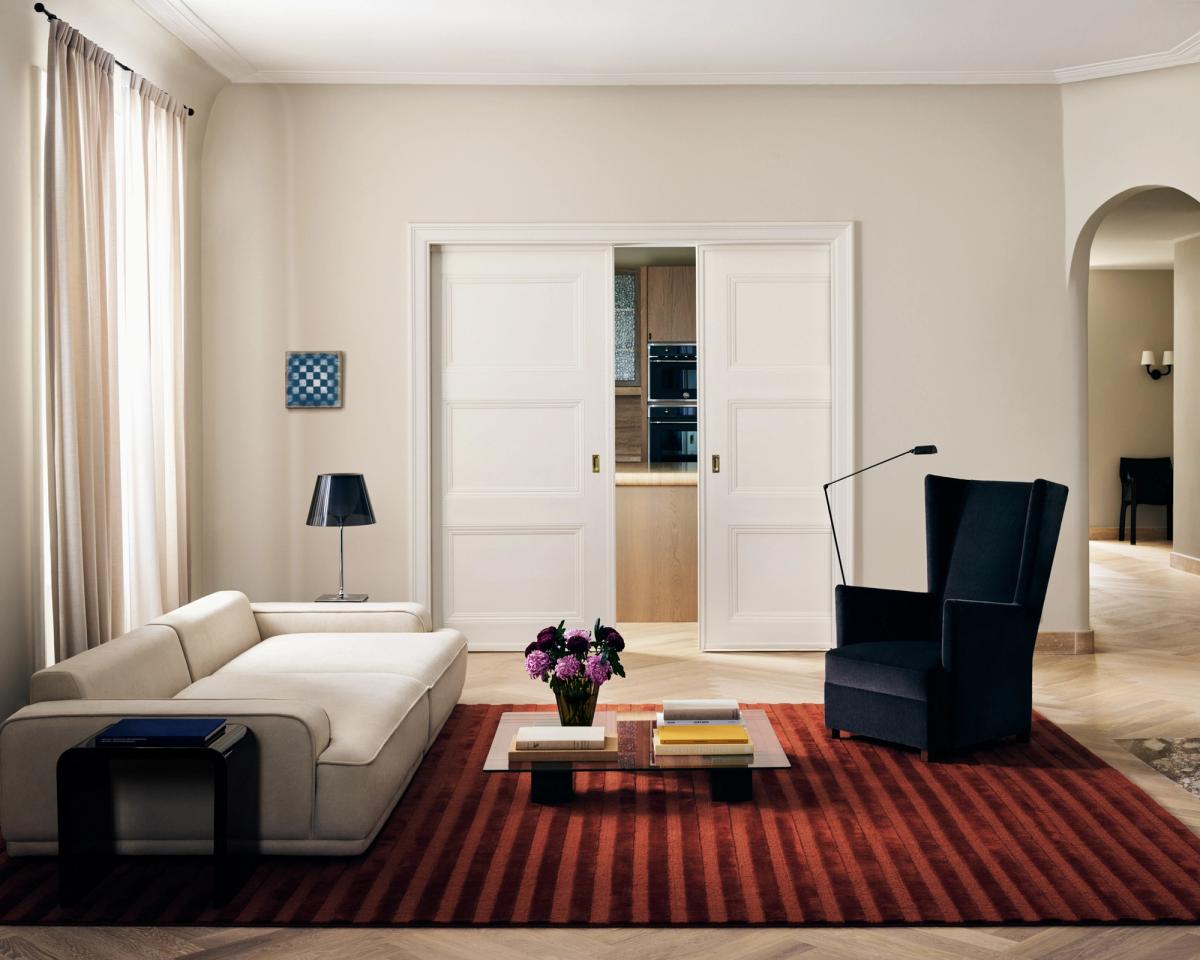 Plüschwollteppich Park 03 in Burgundy, abgebildet in einer hellen Stockholmer Wohnung mit einem großen navyfarbenen Sessel und einem weißen Sofa.