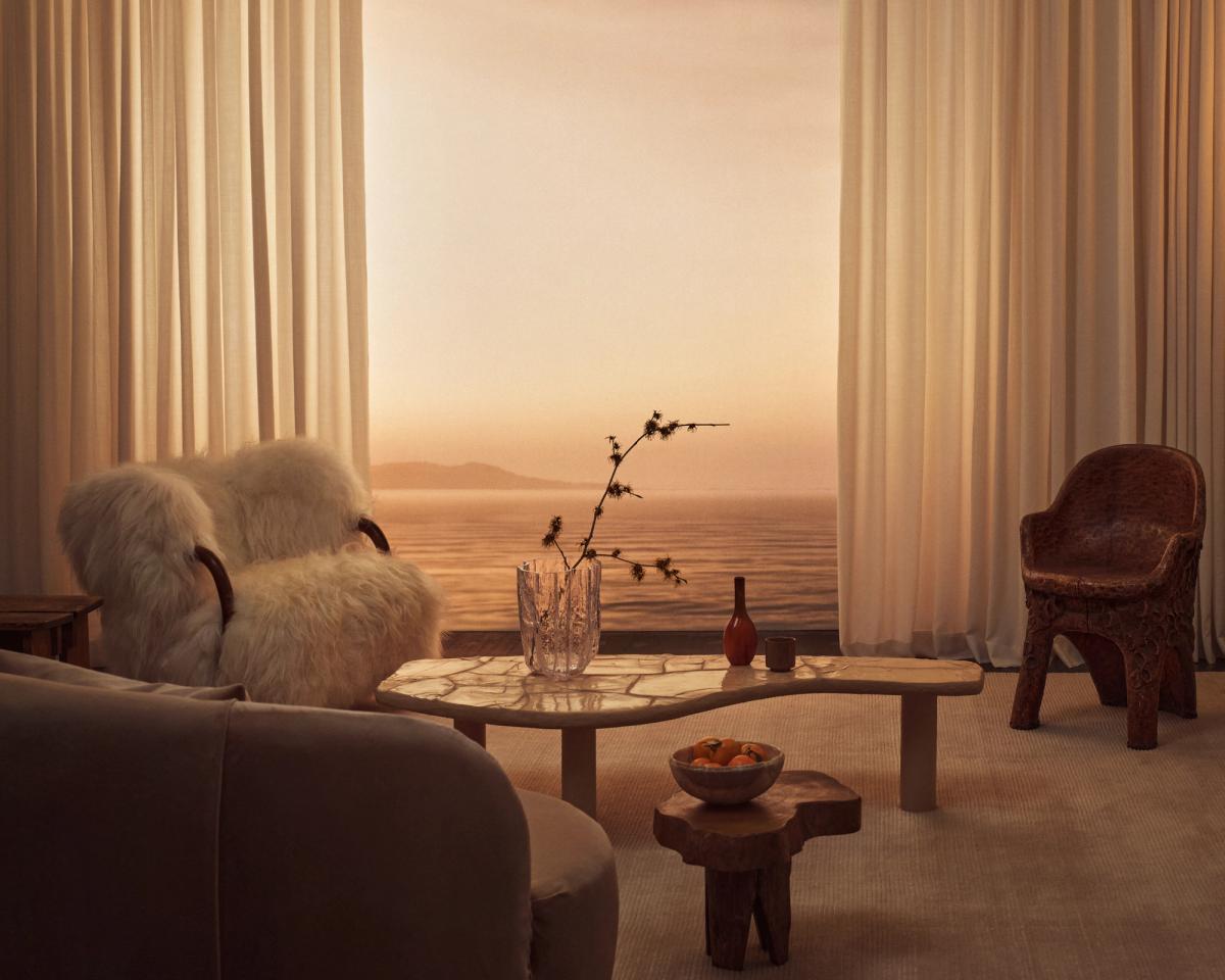 Les rideaux Grand en Perfect White photographiés dans un salon avec des meubles aux tons neutres et de hautes fenêtres donnant sur la mer.