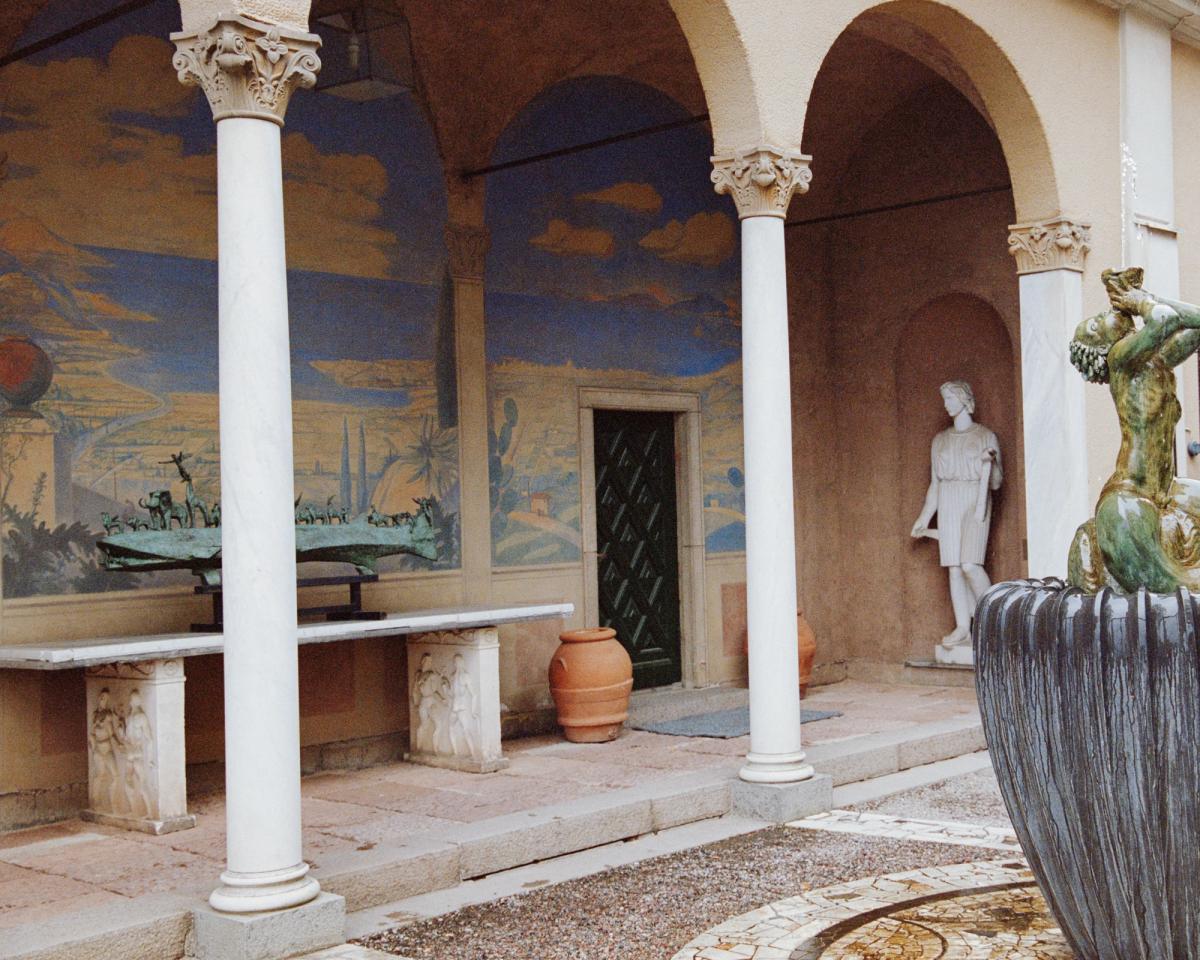 Photo du côté d’un bâtiment dans une cour avec des piliers en pierre et des fresques colorées sur les murs.