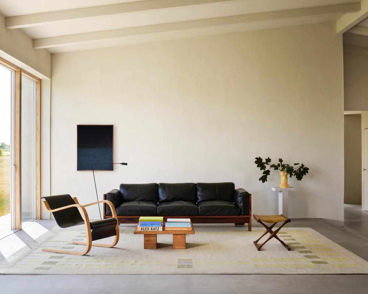 Översiktsbild av ett vardagsrum med mattan Tradition 02 i grönt, omgiven av svarta loungemöbler och ett träbord, som blandar moderna och organiska material.