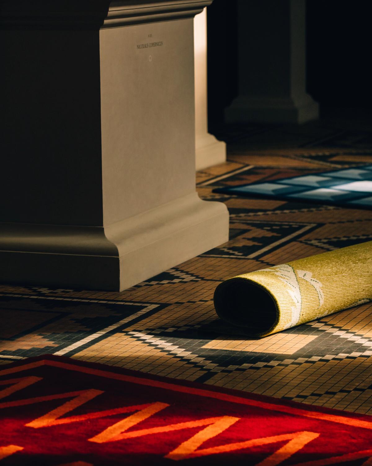Gros plan du tapis en laine moelleux Folding Ribbon - Burgundy de la collection Campbell Rey 2023, photographié sur un sol coloré à motifs au musée Thorvaldsen au Danemark.