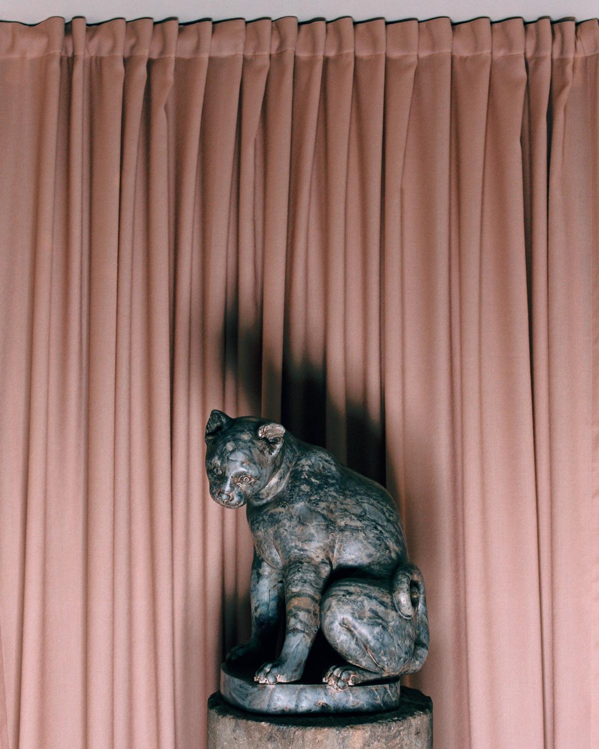 The Grand curtain in Old Rose hanging behind a statue of a cat, adding softness to Galerie Chenel in Paris.