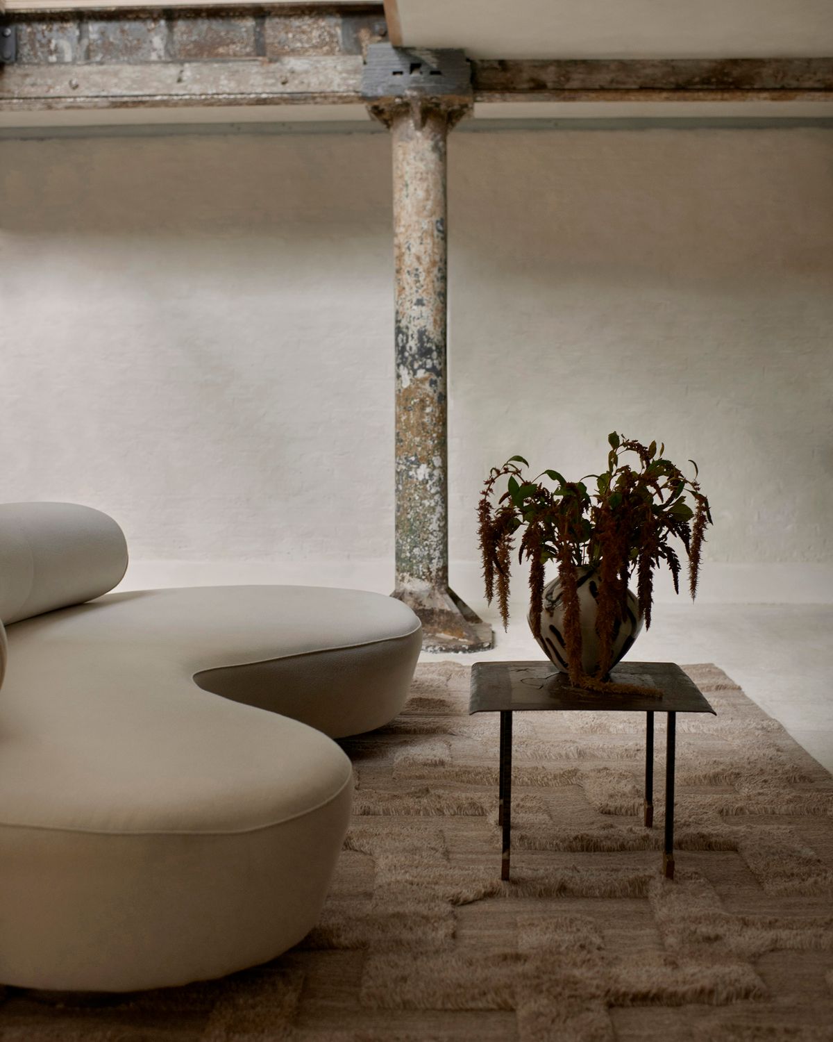 Ryamattan Boho Brown Mix fotograferad i en lounge i modern brutalistisk stil med arkitektoniska metalldetaljer och en mjuk vit soffa i London.