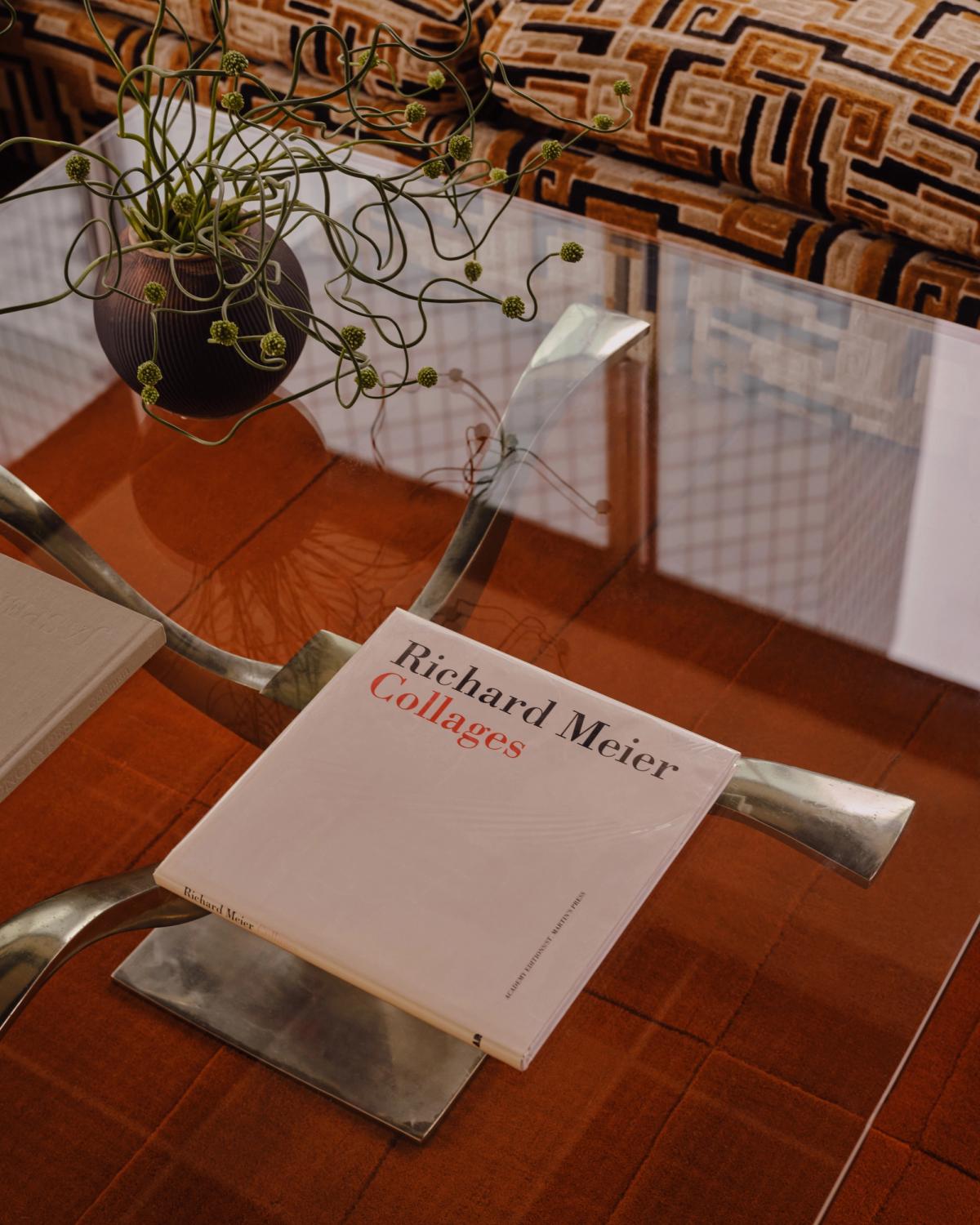 Mattan Lux 2 i färgen Burnt Orange ligger under ett skulpturalt soffbord i glas med metallram, bredvid en brunt mönstrad soffa.