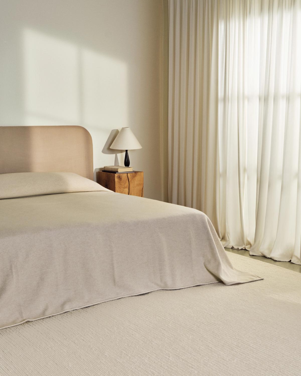 Tapis en laine tissé à plat Braid en Cream photographié dans une chambre avec un cadre de lit beige et les rideaux The Grand.