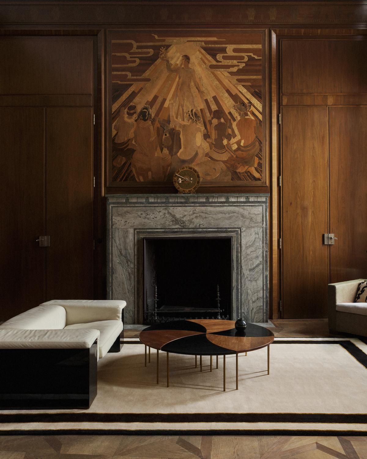 Plüschwollteppich Gild 01, abgebildet in einem eleganten Wohnzimmer mit hohen Holzwänden und einem prächtigen Marmorkamin.