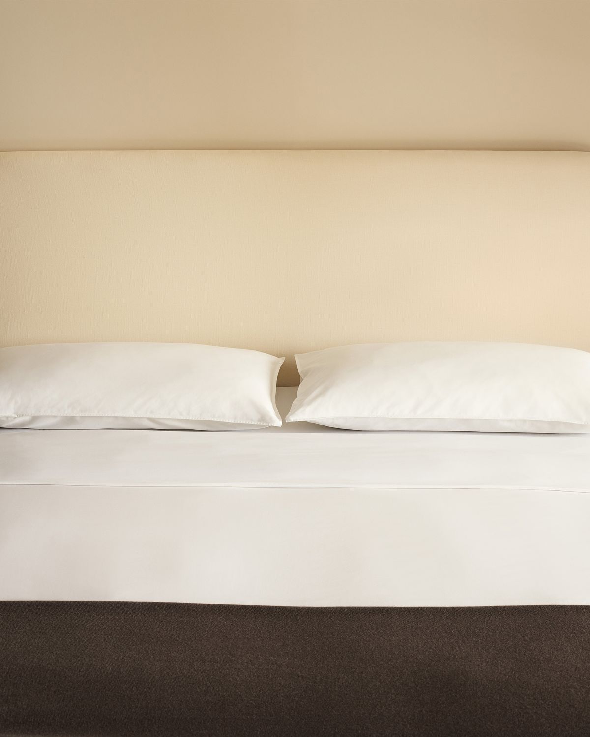 Crisp white bedding styled with the Signature Headboard in Warm White and a Heritage throw in Taupe, photographed straight on.