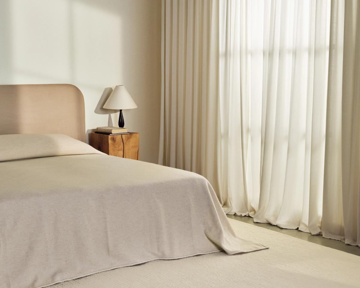 Tapis en laine tissé à plat Braid en Cream photographié dans une chambre avec des rideaux couleur crème et un lit assorti.