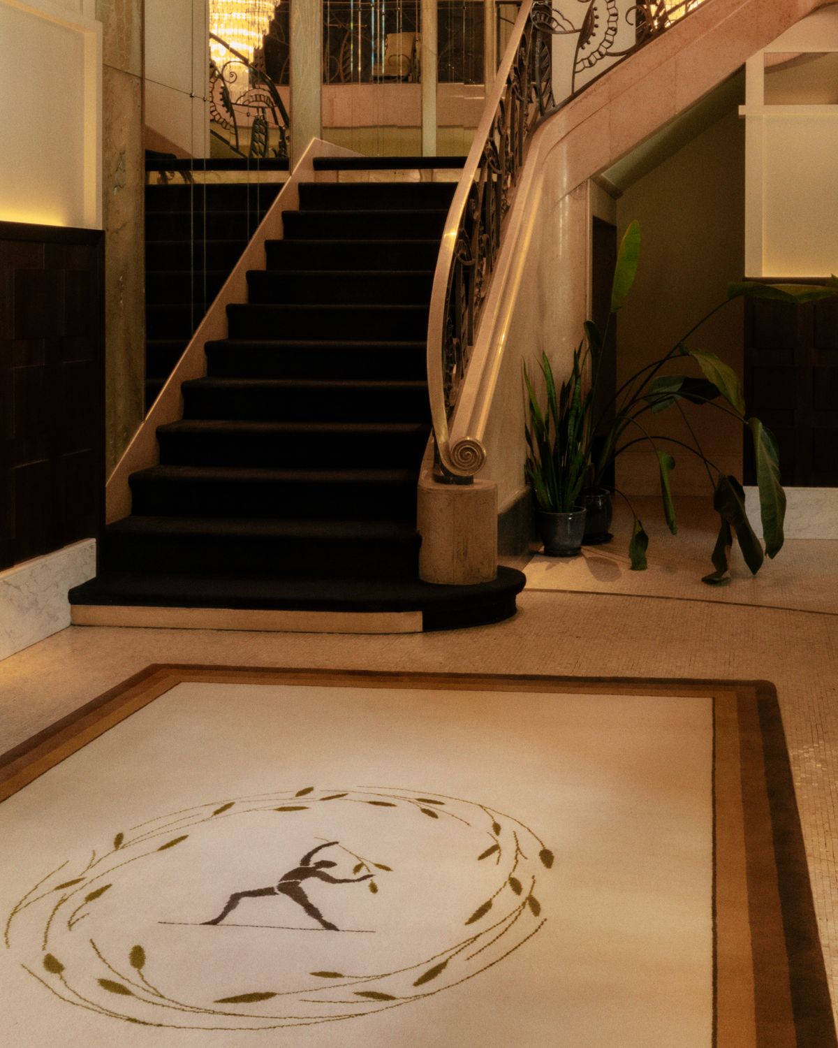 Plush wool rug designed by Parisian designer Fabrizio Casiraghi on a marble floor next to a beautiful staircase and large mirrors that reflect a lit chandelier in Paris, France