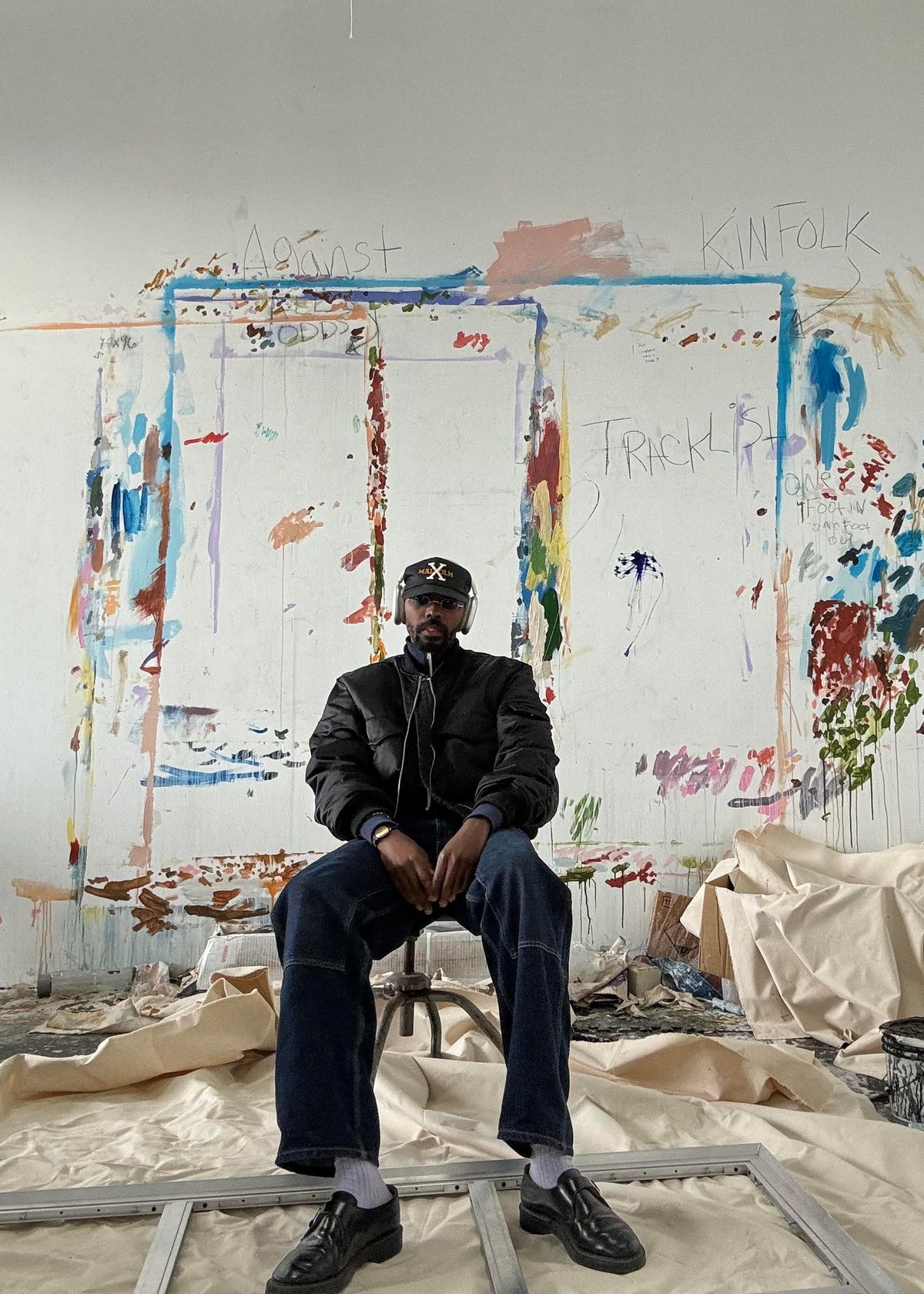 Portrait of Sissòn in front of a painted wall in an art studio.