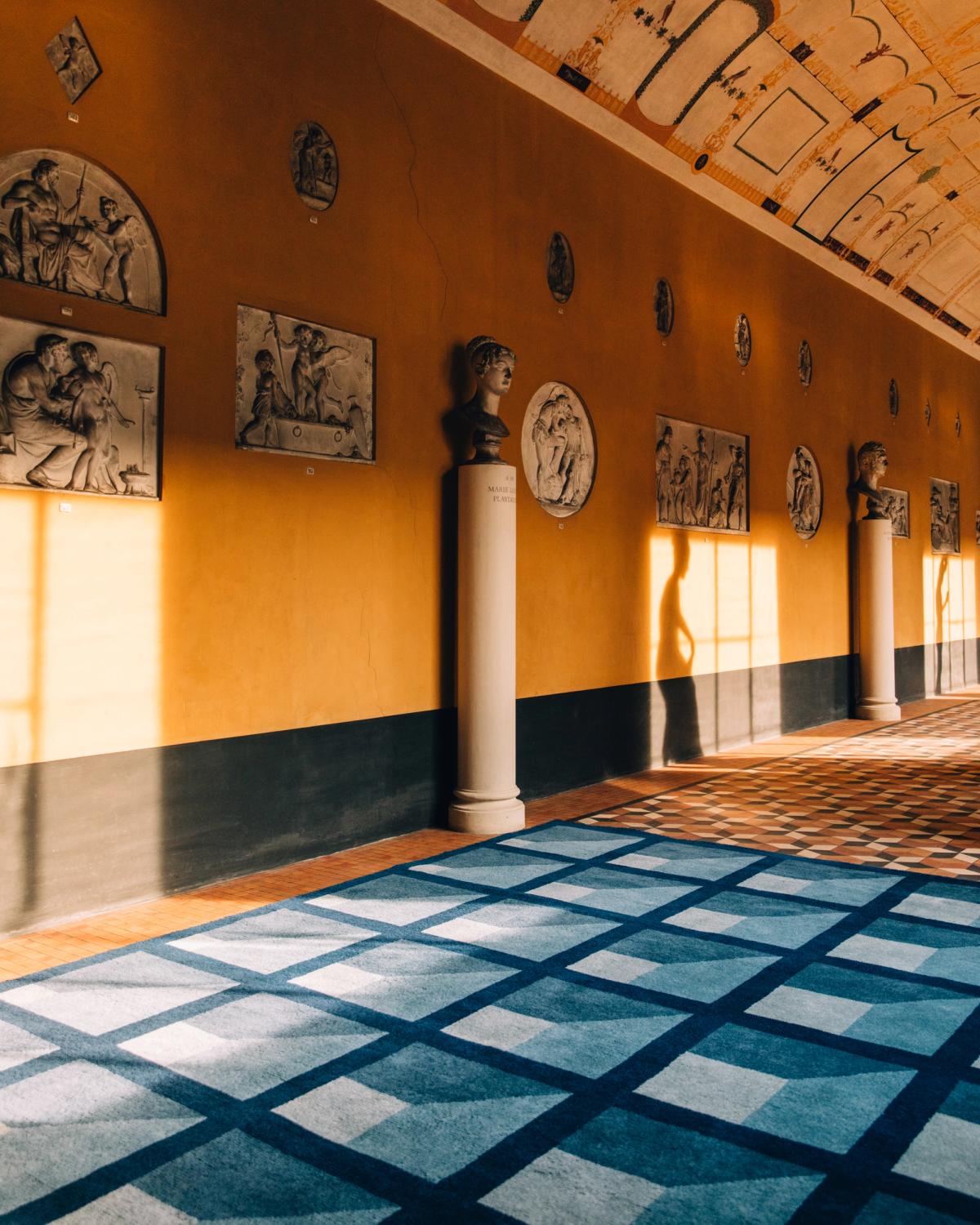 Tapis en laine moelleux Garden Maze - Blue de la collection Campbell Rey 2023 photographié dans un grand hall avec de magnifiques statues en marbre au musée Thorvaldsen au Danemark.